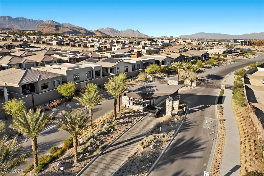 Aerial view of a desert neighborhood with a landscaped entrance, contemporary homes, and distant mountains.