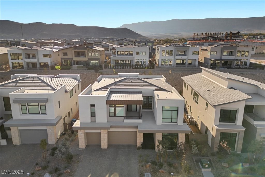 Modern white home with a three-car garage, seen from above with mountains beyond.