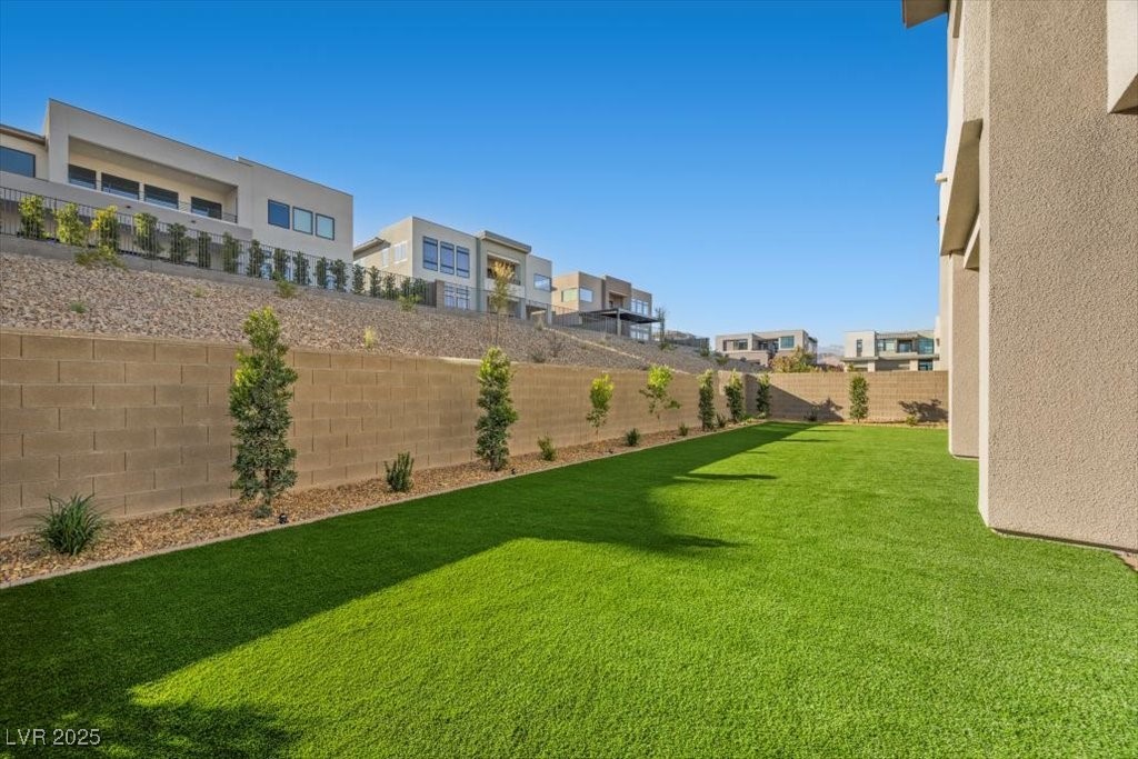 Backyard lawn bordered by a block wall, young trees, and neighboring modern homes.