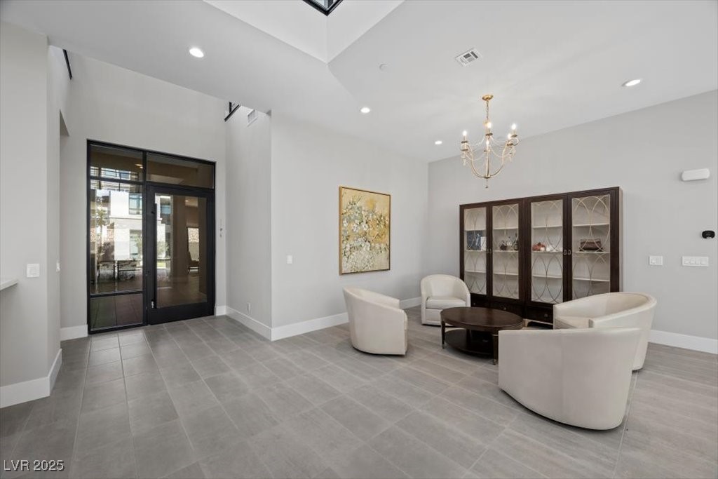 Furnished sitting area with high ceilings, black-framed glass doors, and cream chairs around a coffee table.