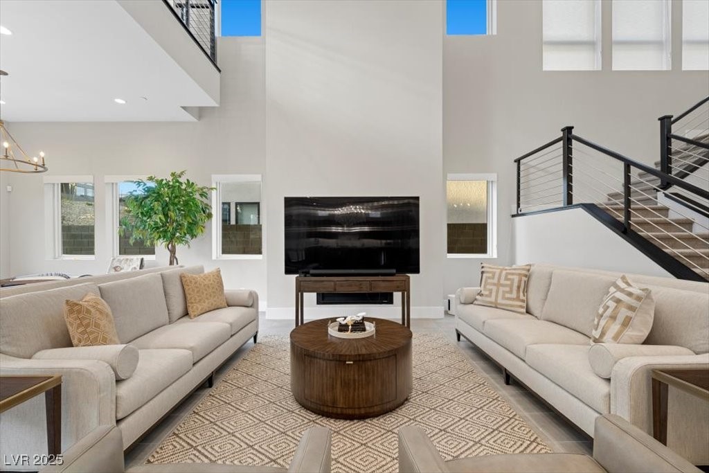 Furnished double-height living room with paired sofas, a round coffee table, and a black-railed staircase.