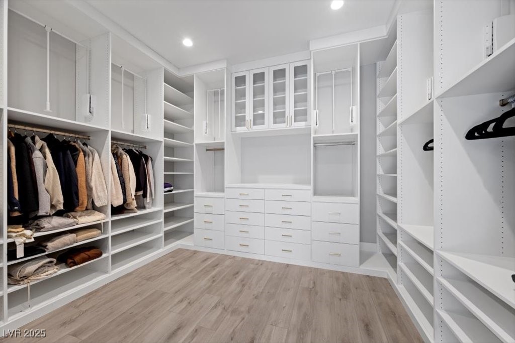 Walk-in closet with white built-ins, glass-front cabinets, drawers, and hanging clothes.