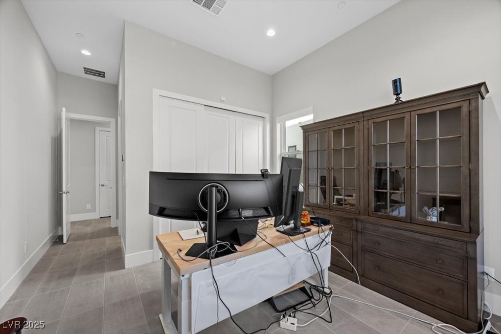 Home office with multiple monitors, a dark wood glass-front cabinet, and gray tile floor.