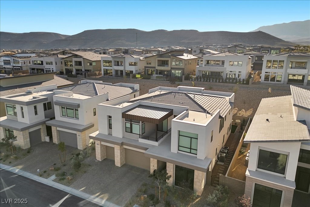 Modern white two-story home in a Las Vegas neighborhood, with neighboring homes and mountains beyond.