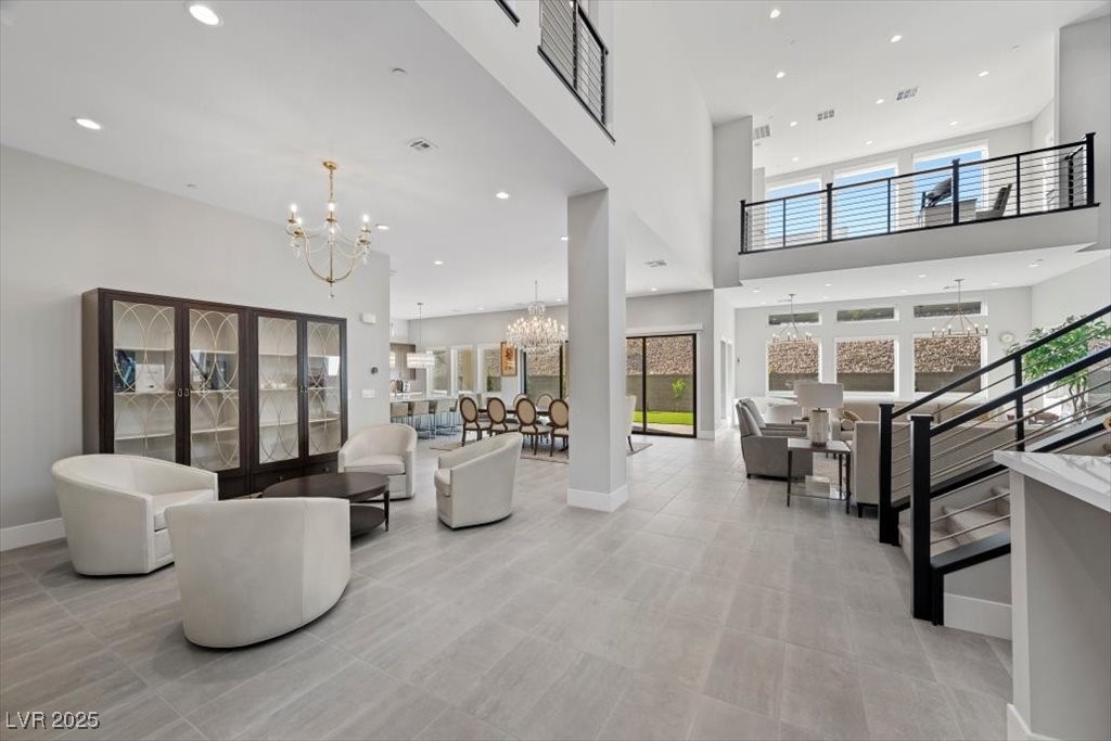 Two-story great room with white lounge chairs, a black-railed staircase, and an upstairs balcony.