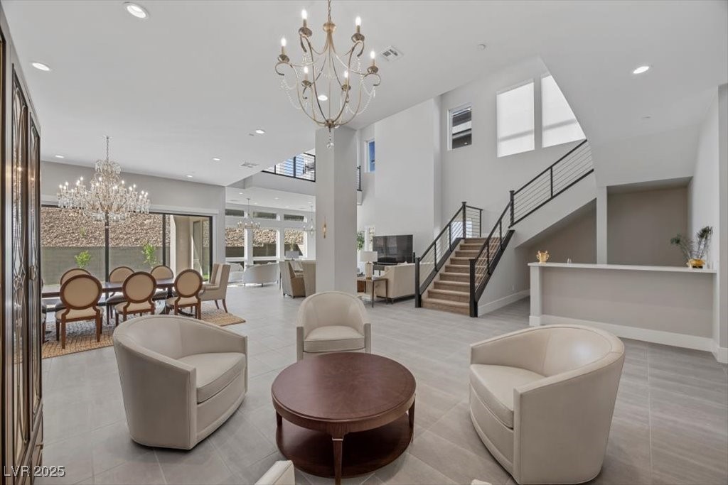 Open-plan living room with curved cream chairs, a dining area, chandelier, and staircase.