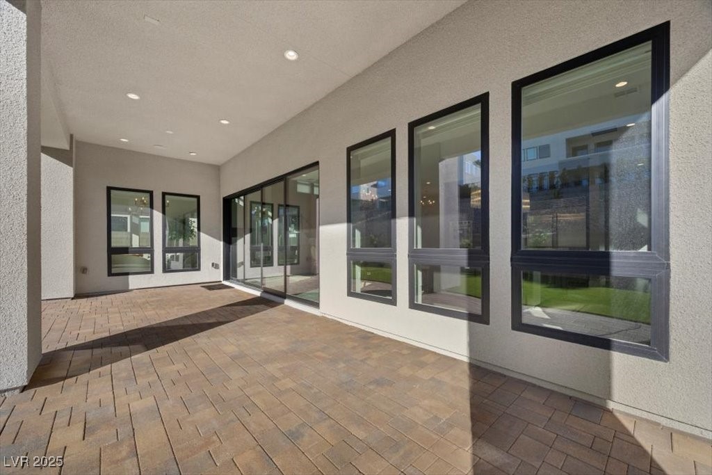 Covered patio with tan pavers, dark-framed windows, and sliding glass doors.