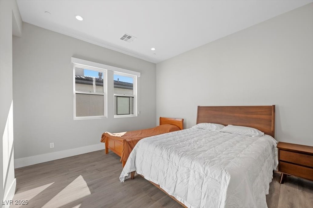 Bedroom with a large white-covered bed, smaller bed, wood furnishings, and two windows.
