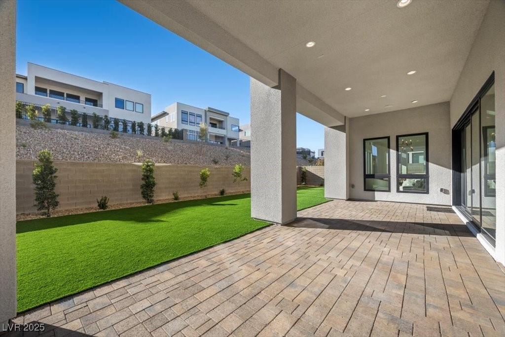 Covered patio with tan pavers and recessed lights beside a green lawn.