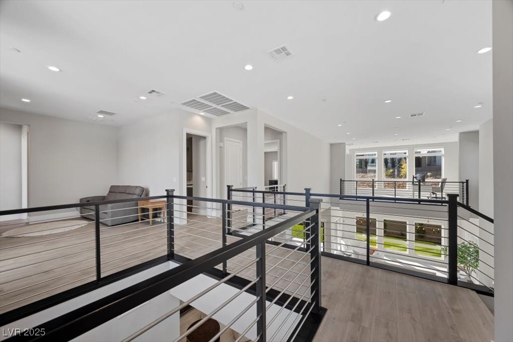 Upstairs landing overlooking the living area, with black cable railings, light wood floors, and a gray sofa.