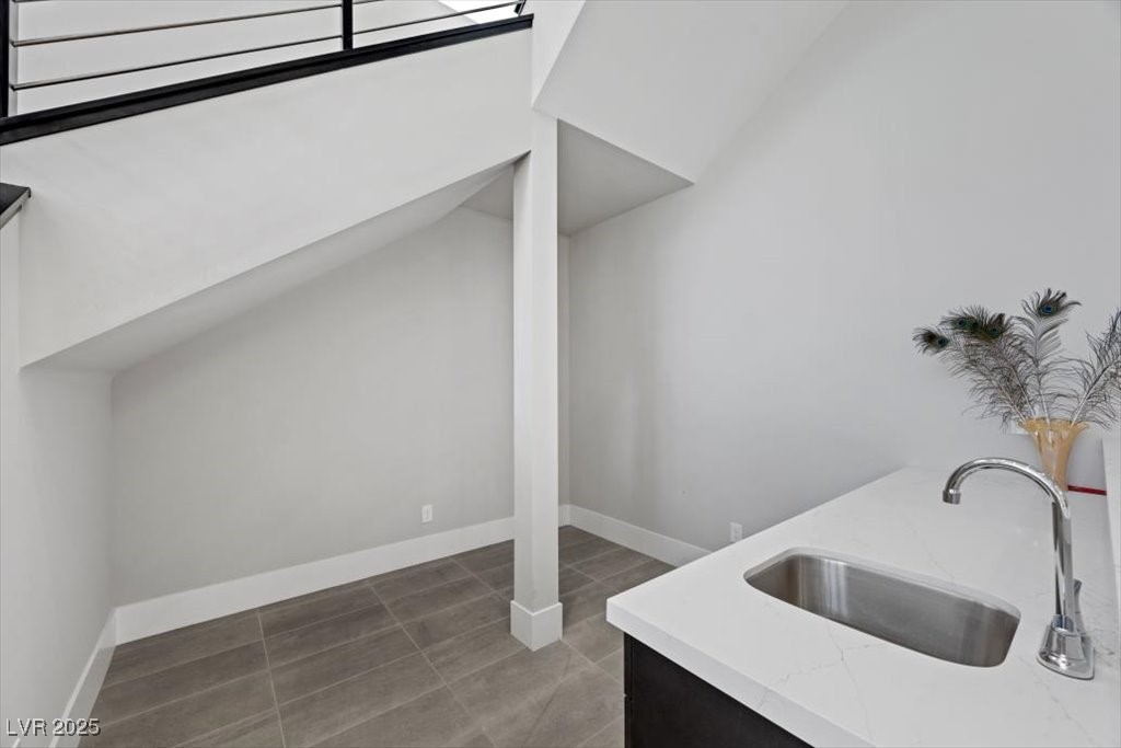 Modern kitchen sink and white counter beside a tiled floor and staircase.