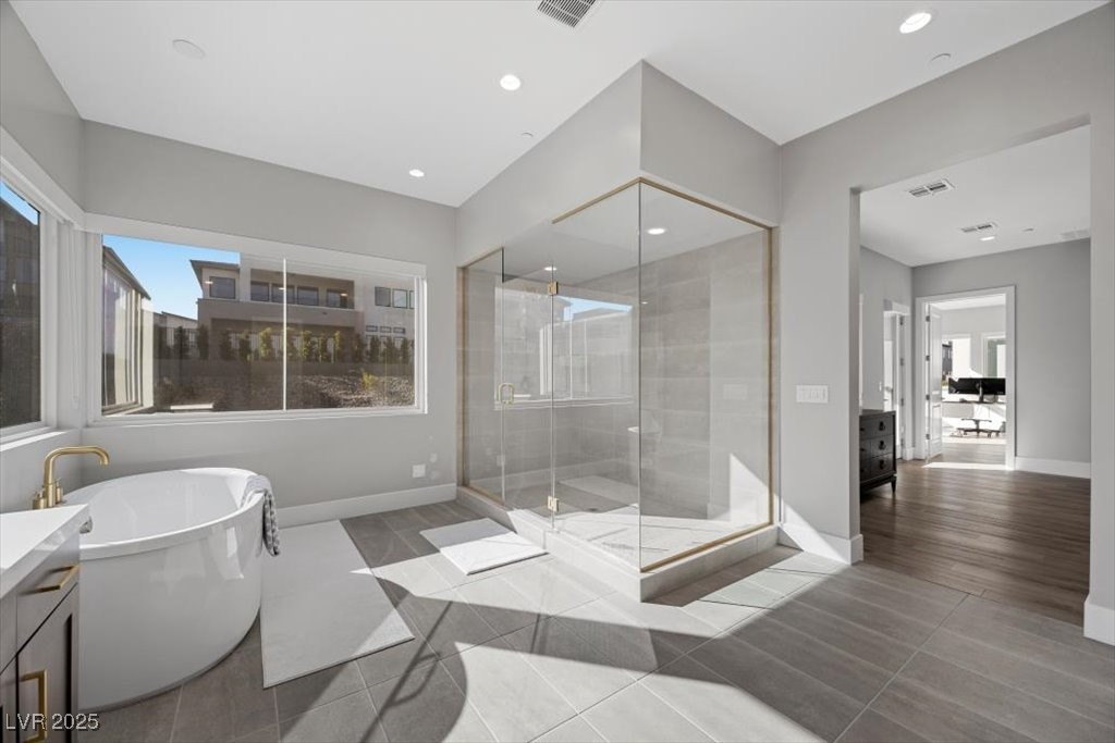 Modern bathroom with a freestanding tub beside a brass-trimmed glass shower and large window.
