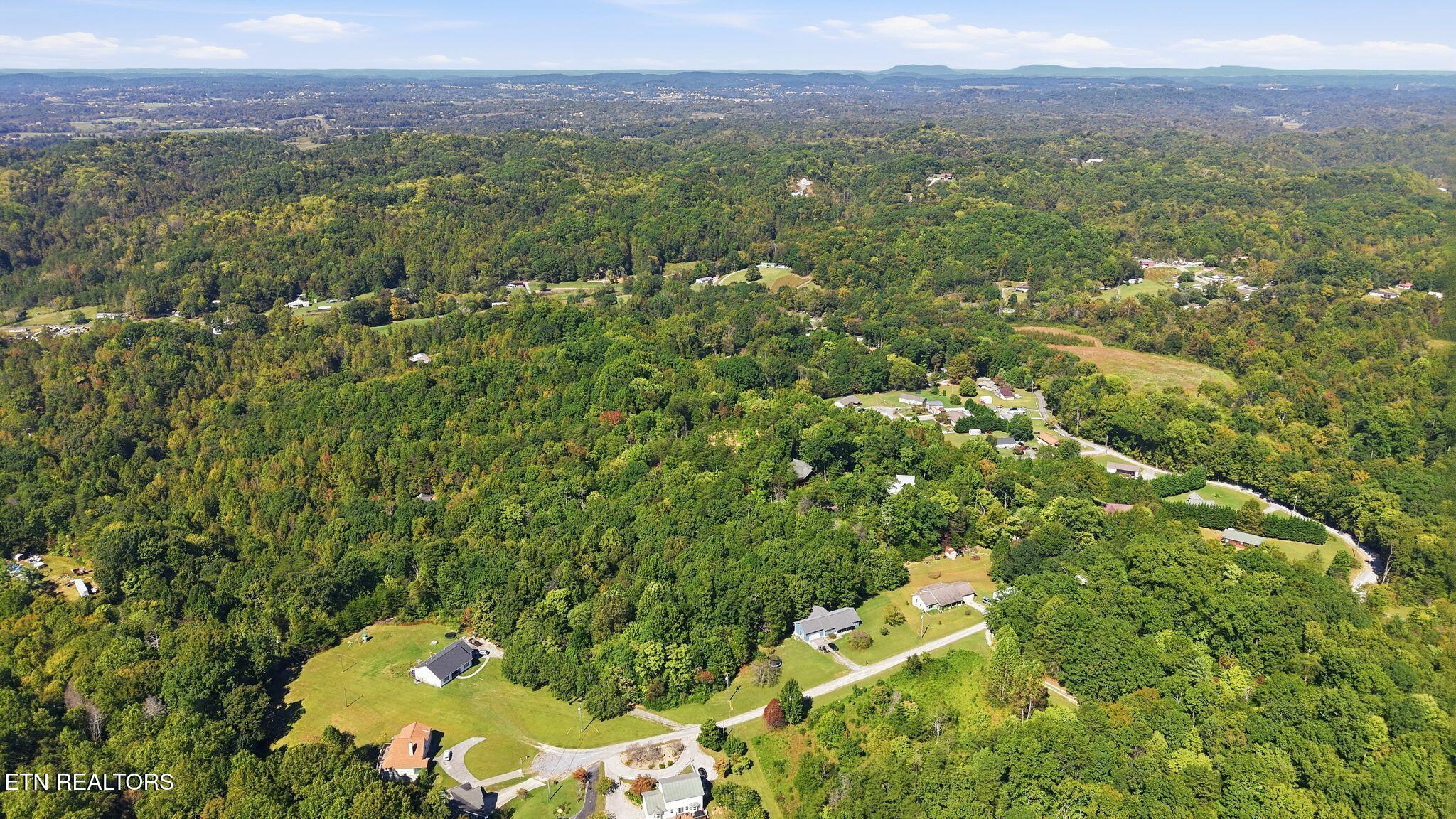 Aerial view of wooded rural land with scattered homes, winding roads, and distant ridgelines.