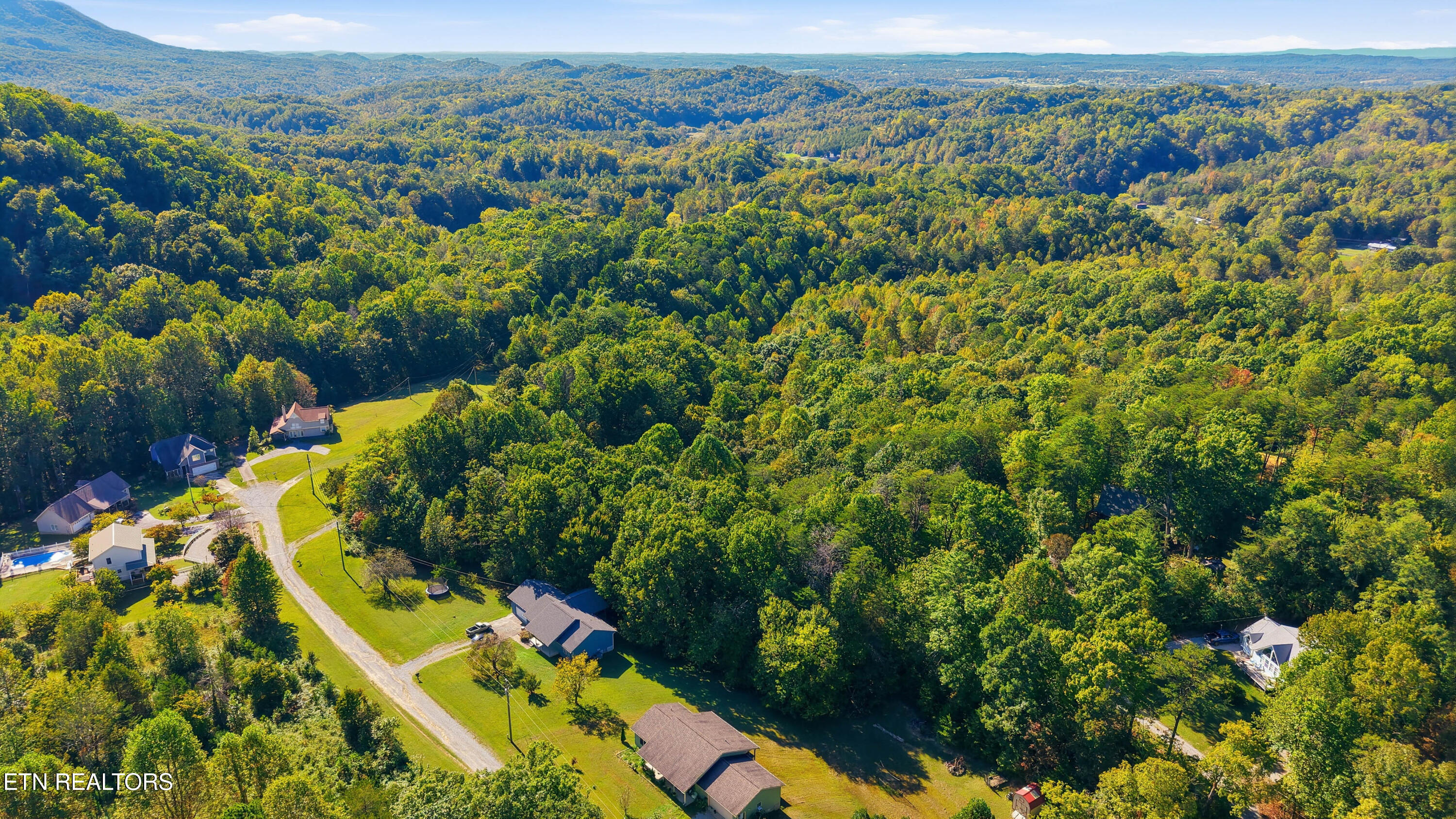 Aerial view of wooded rolling hills, scattered homes, and a gravel road.