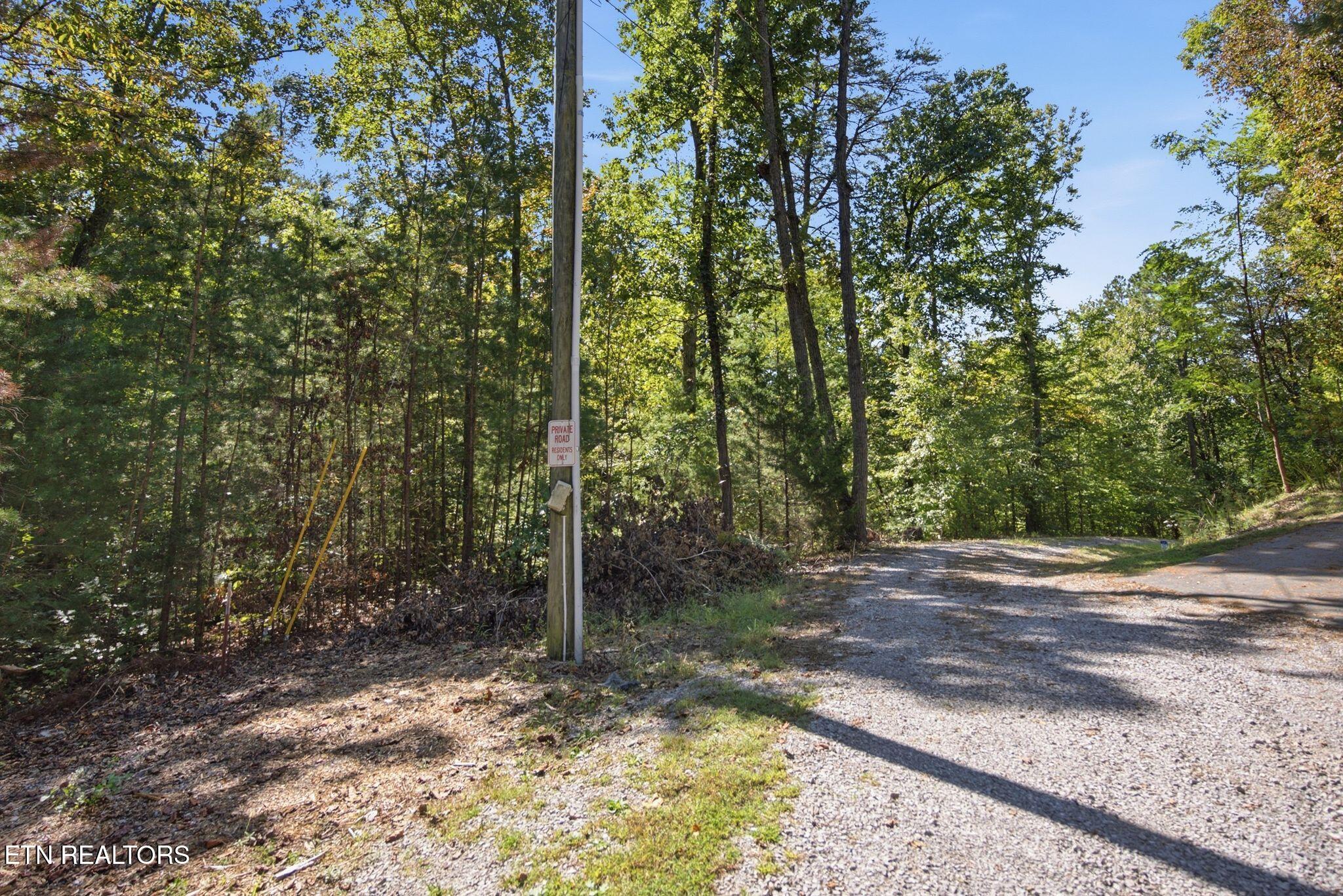 Gravel private road curves through dense woods beside a residents-only sign.