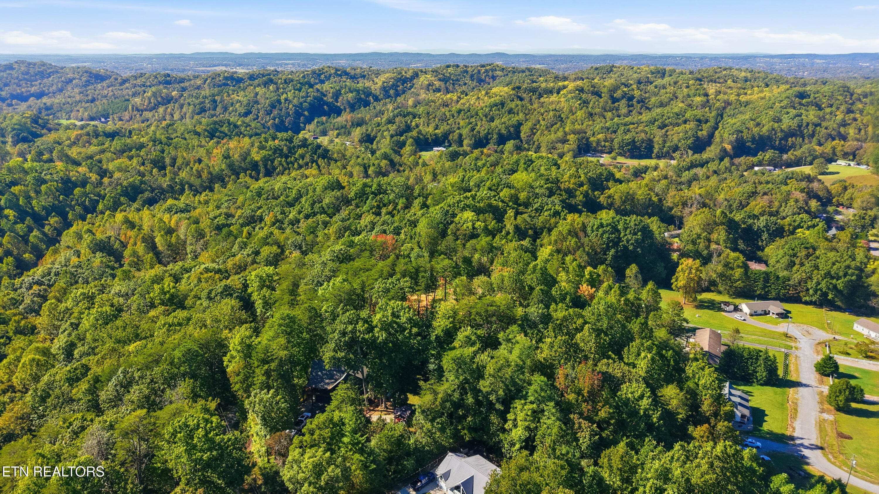 Aerial view of wooded hills and scattered homes, with a rural road and distant ridgelines.