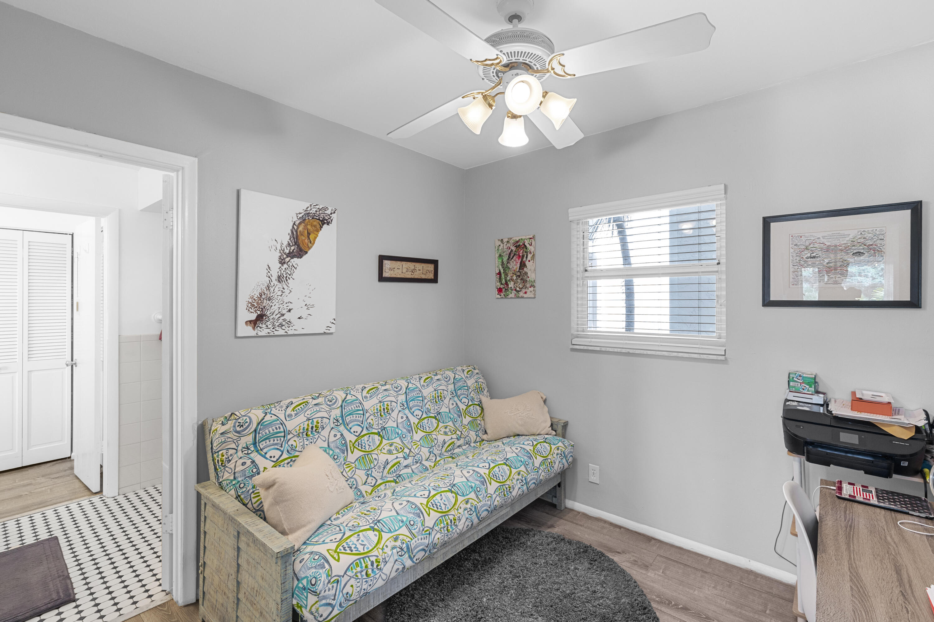Furnished room with a colorful patterned sofa bed, ceiling fan, and window with blinds.
