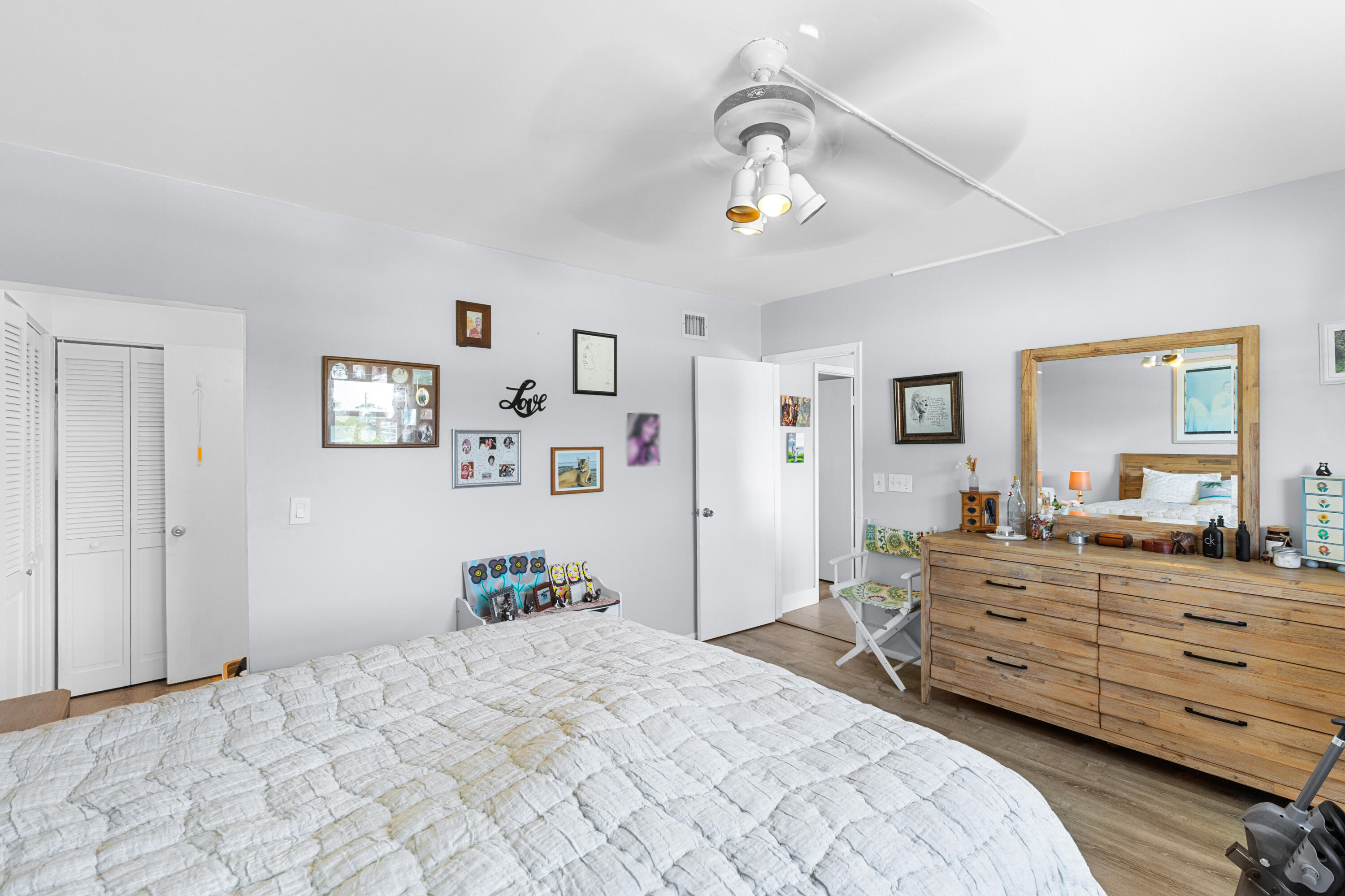Bedroom with a white quilted bed and a long wooden dresser beneath a framed mirror.
