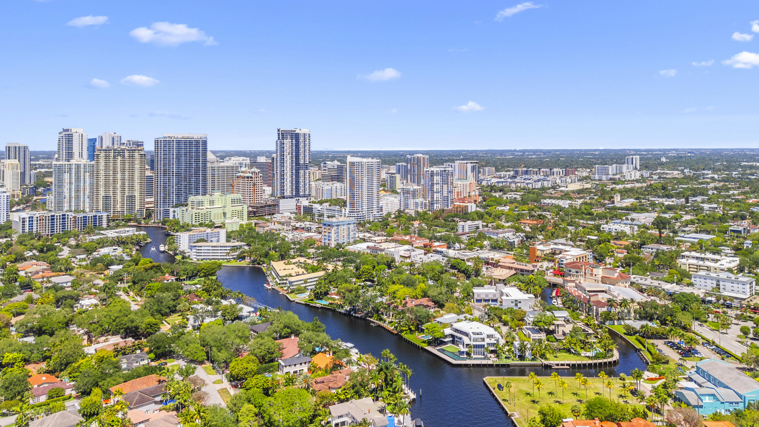 Aerial view of Fort Lauderdale high-rises beyond a winding canal and waterfront homes.