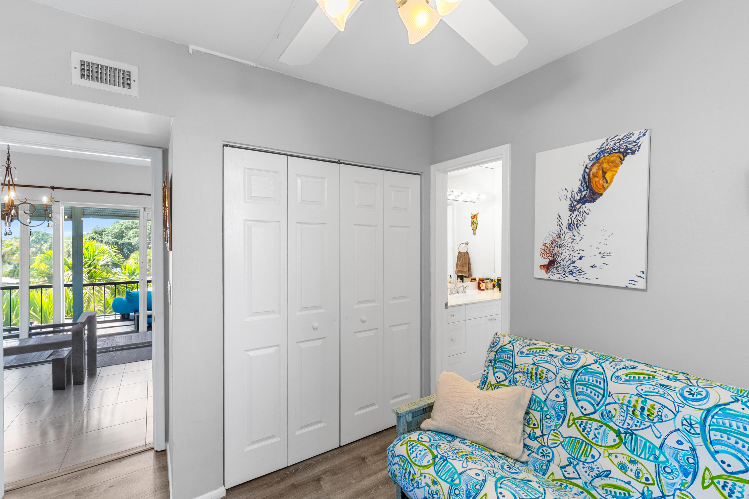 Furnished room with a colorful patterned sofa, closet doors, and a balcony framed by tropical greenery.