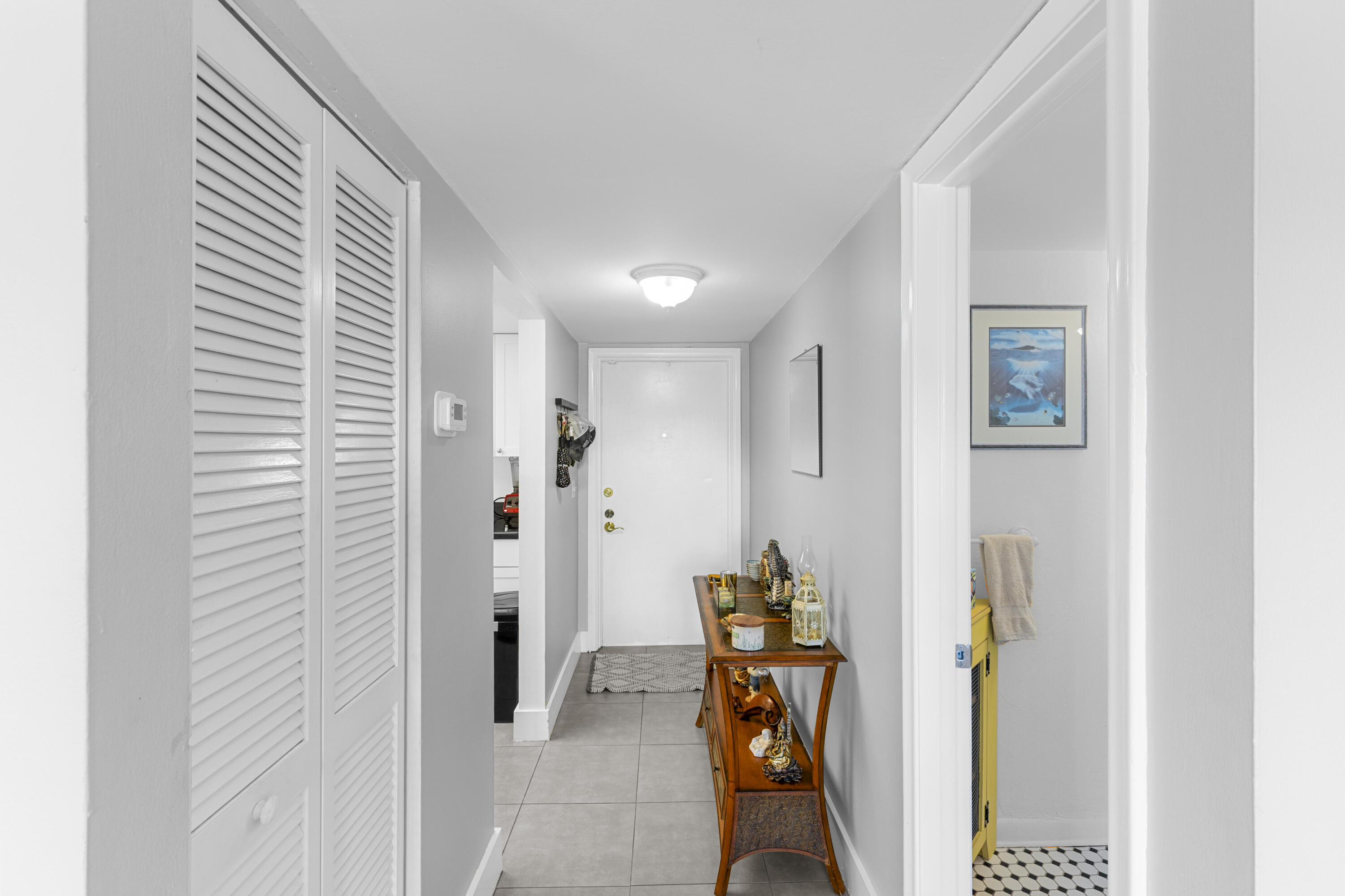 Apartment entry hallway with gray tile floors, louvered closet doors, and a wooden console table.