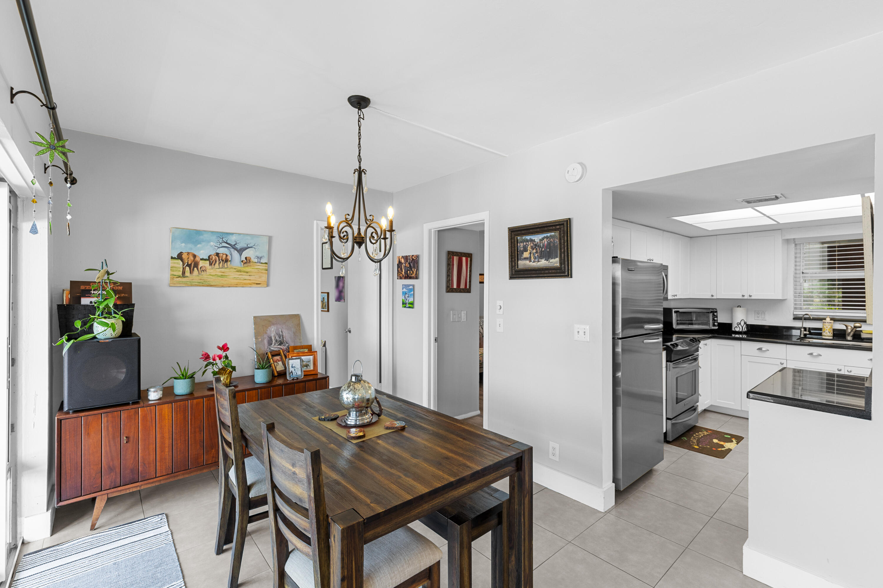 Dining room with a dark wood table, chandelier, sideboard, and an adjoining white kitchen.