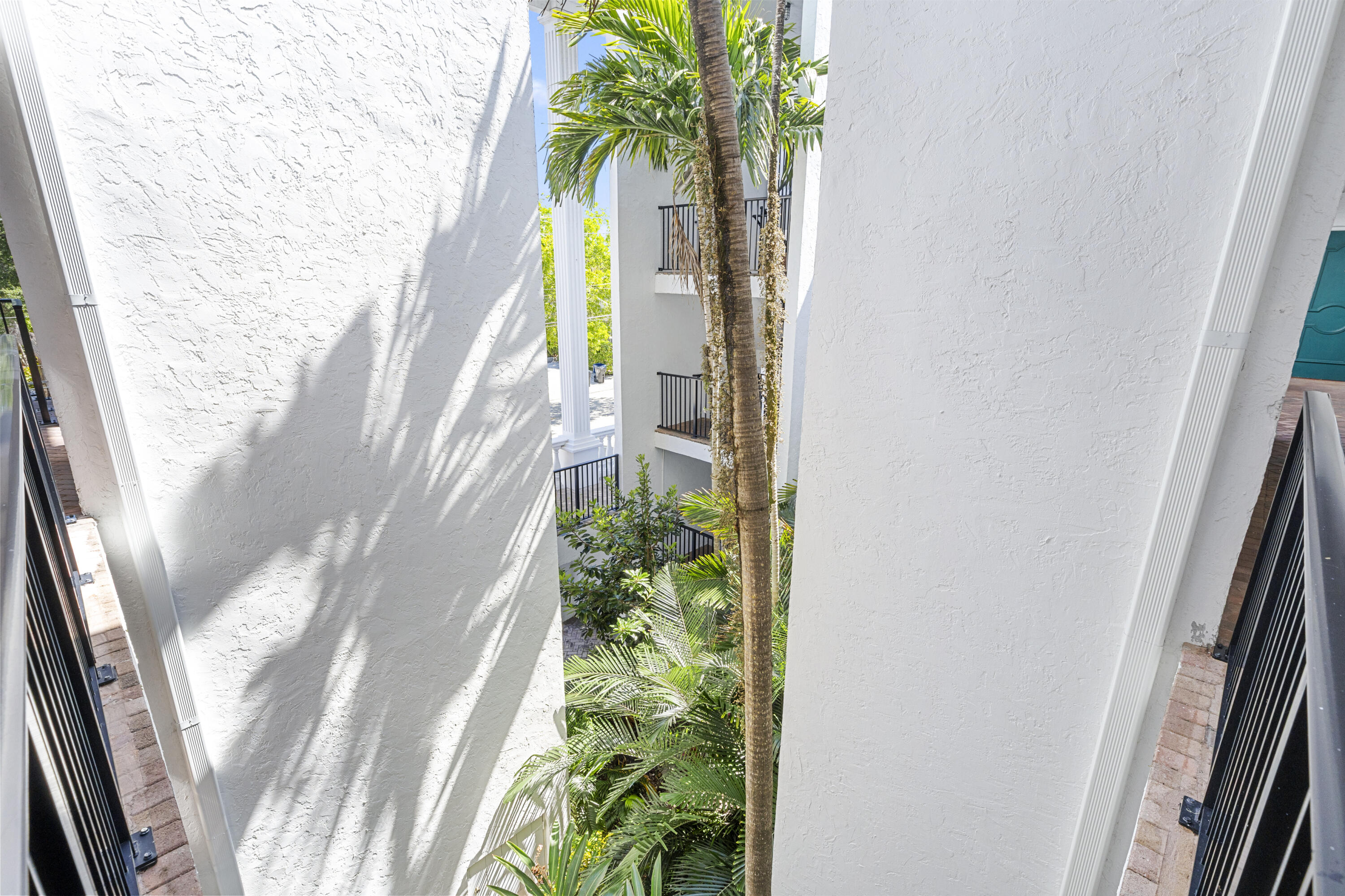 White stucco courtyard framed by palm trees, with black railings and brick walkways.