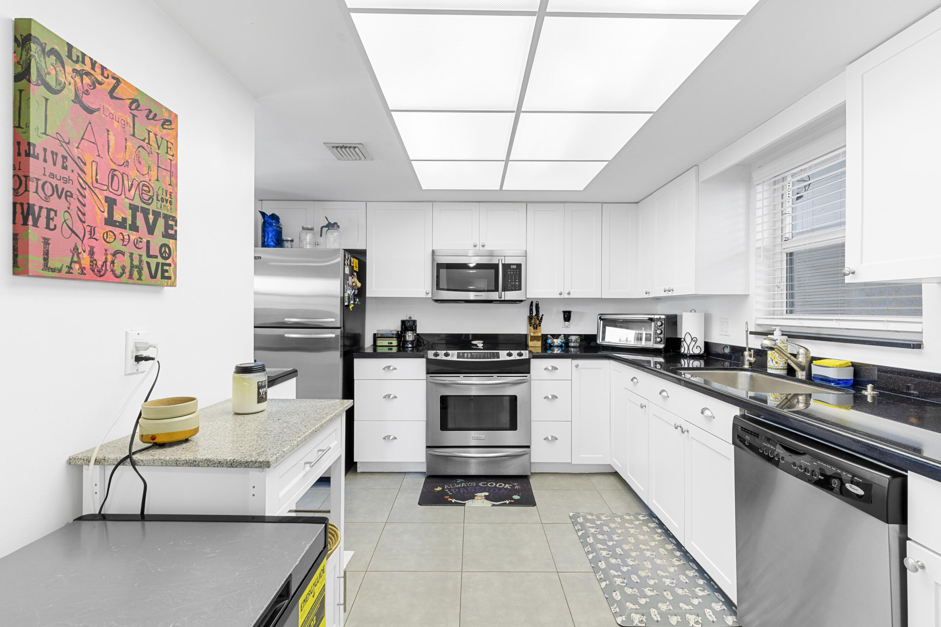 Kitchen with white cabinetry, black countertops, stainless steel appliances, and a sink beneath a window.
