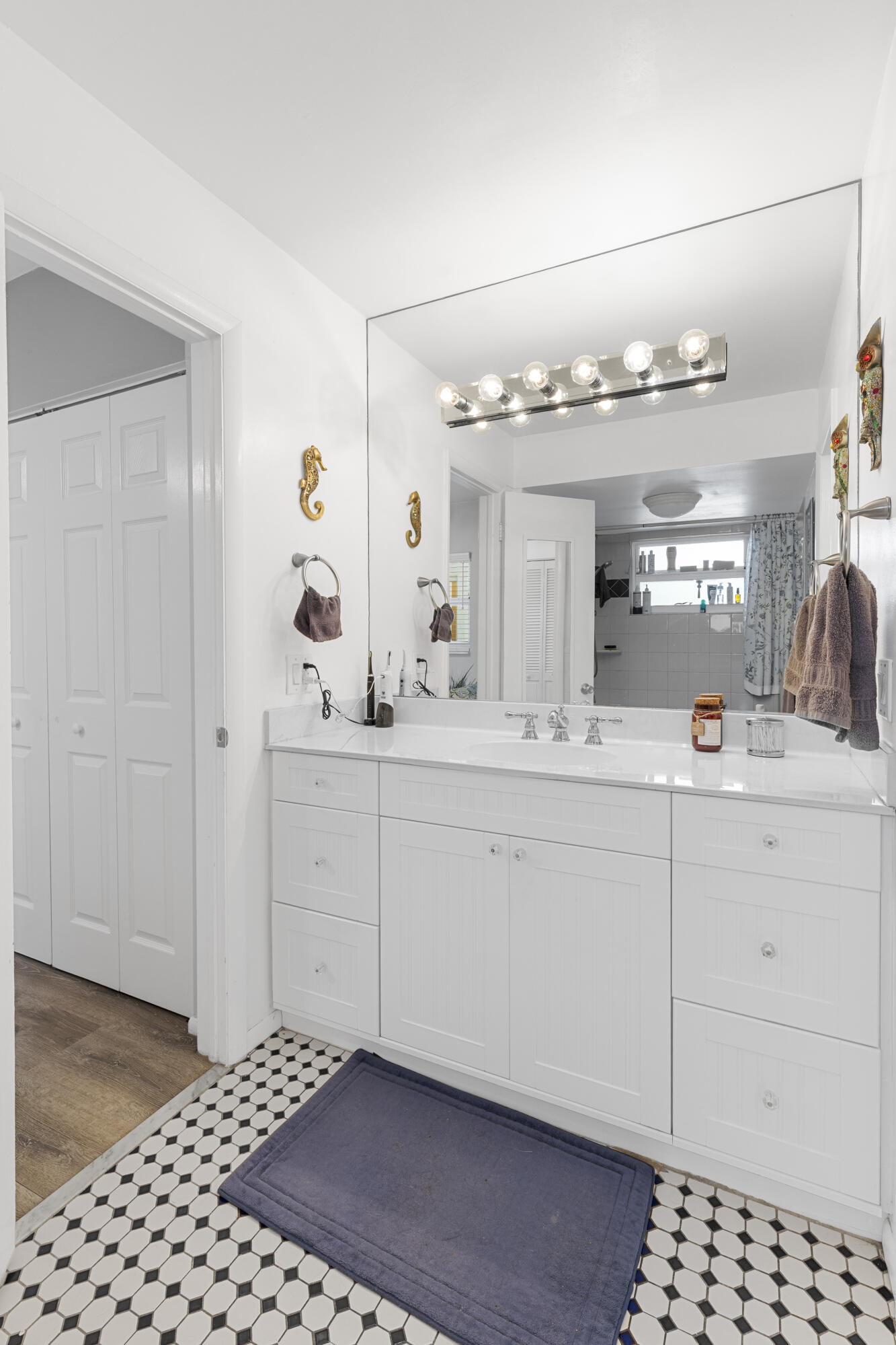 Bathroom vanity with a large mirror, white cabinetry, and black-and-white geometric floor tiles.
