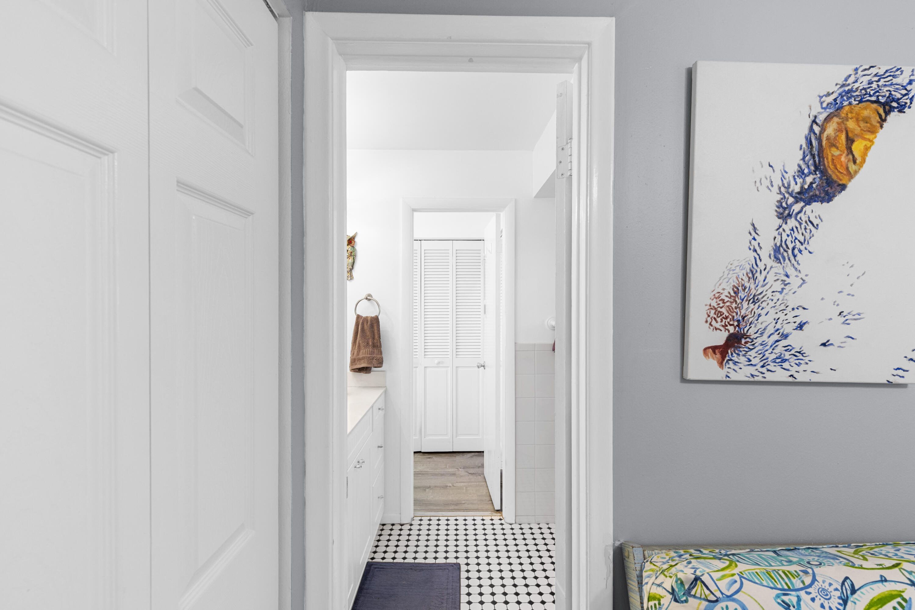 White hallway with geometric tile leading to a bathroom, beside colorful fish artwork.