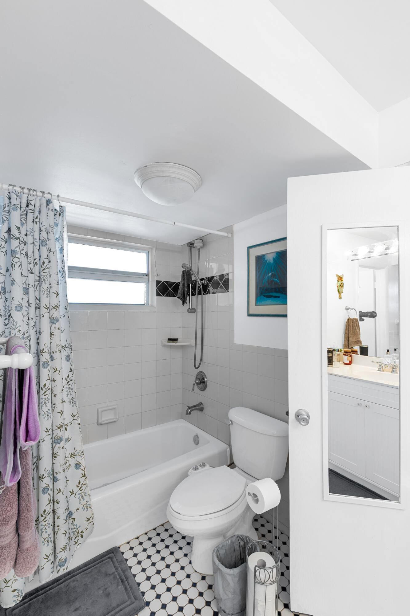 Bathroom with a bathtub, floral shower curtain, toilet, and black-and-white hexagonal floor tiles.