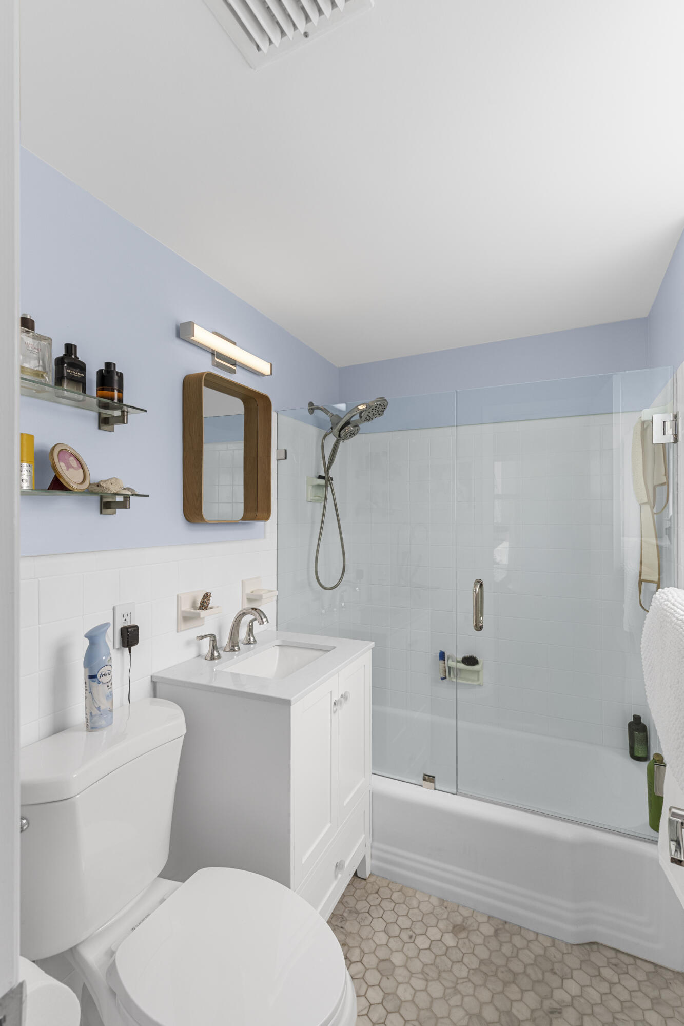 Bathroom with a glass-enclosed tub and shower, white vanity, and hexagonal tile floor.