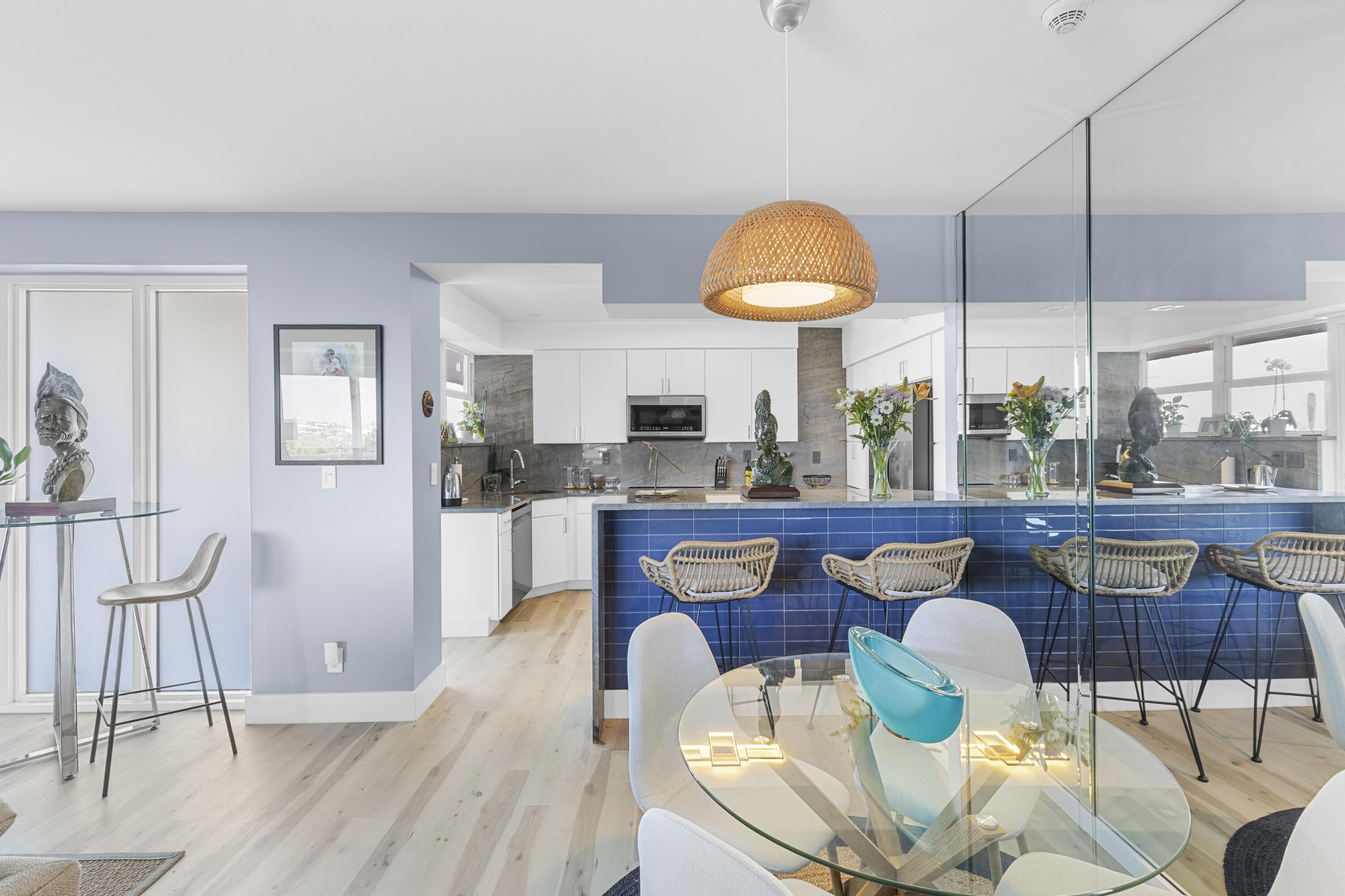 Open kitchen and dining area with a blue-tiled breakfast bar, woven stools, and glass dining table.