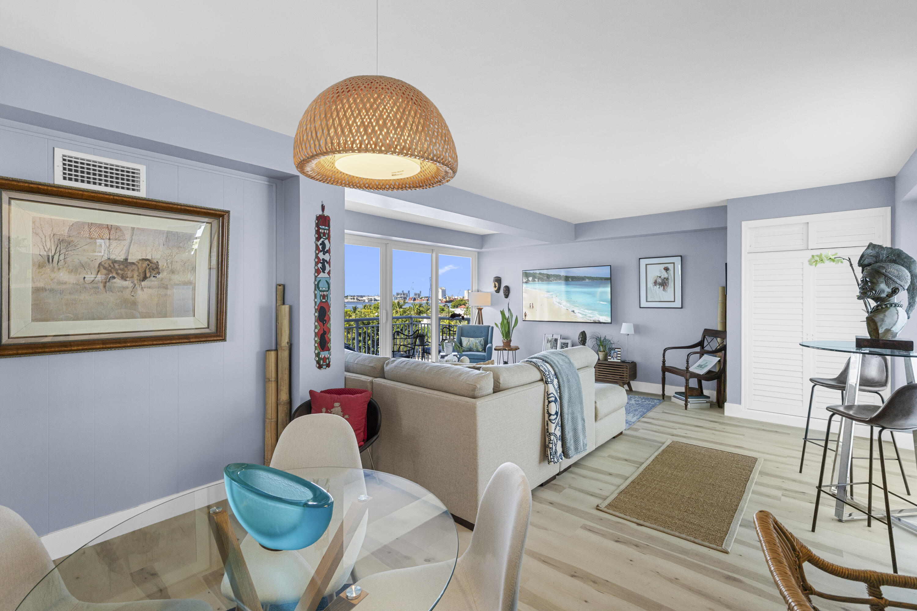 Open-plan living and dining room with balcony views, pale blue walls, and a glass dining table.