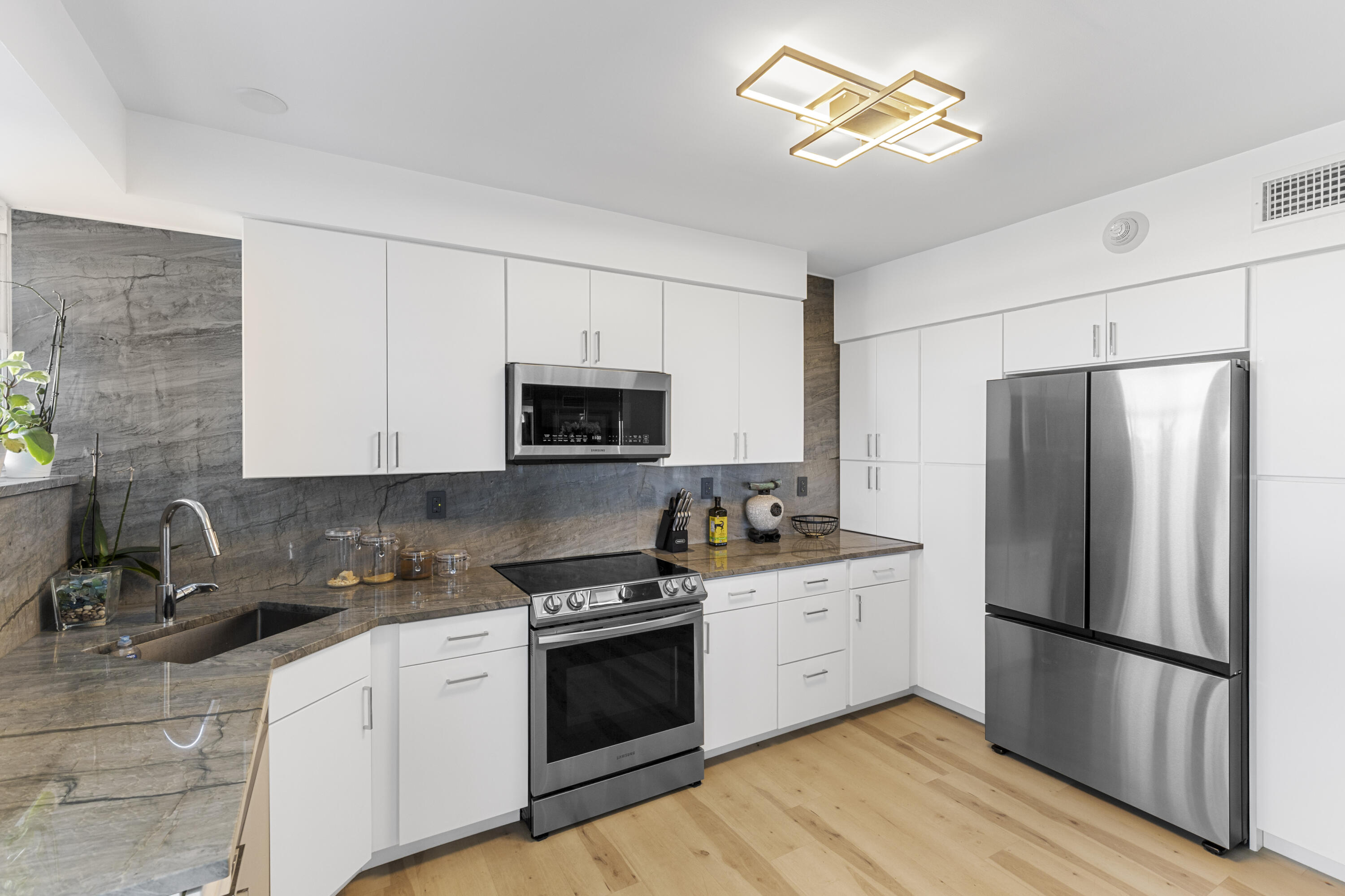 Modern kitchen with white cabinets, stone counters, stainless steel appliances, and light wood flooring.