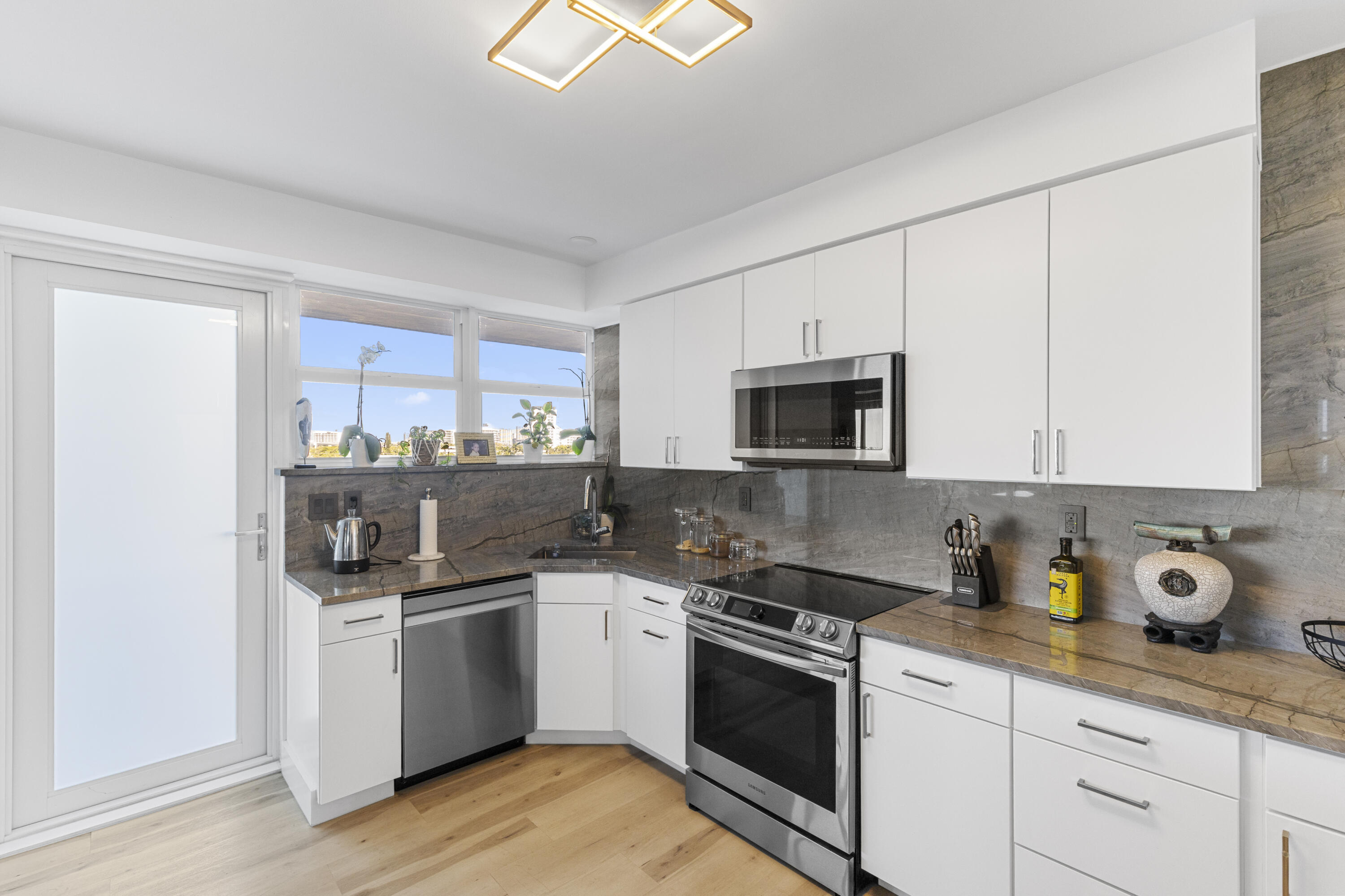 Modern kitchen with white cabinets, stone counters, stainless appliances, and a window over the sink.