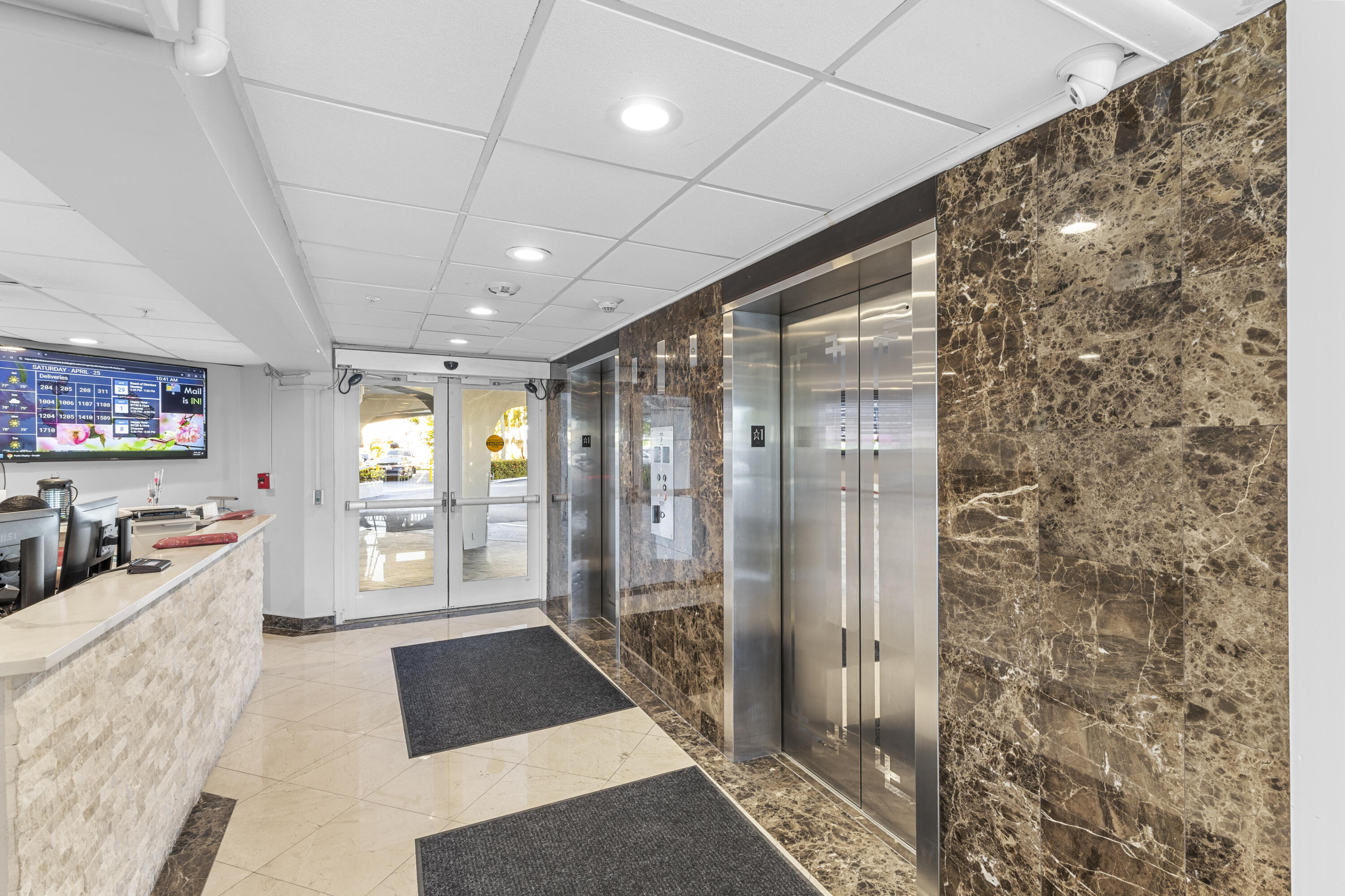 Building lobby with stainless-steel elevators, marble walls, and a reception desk.