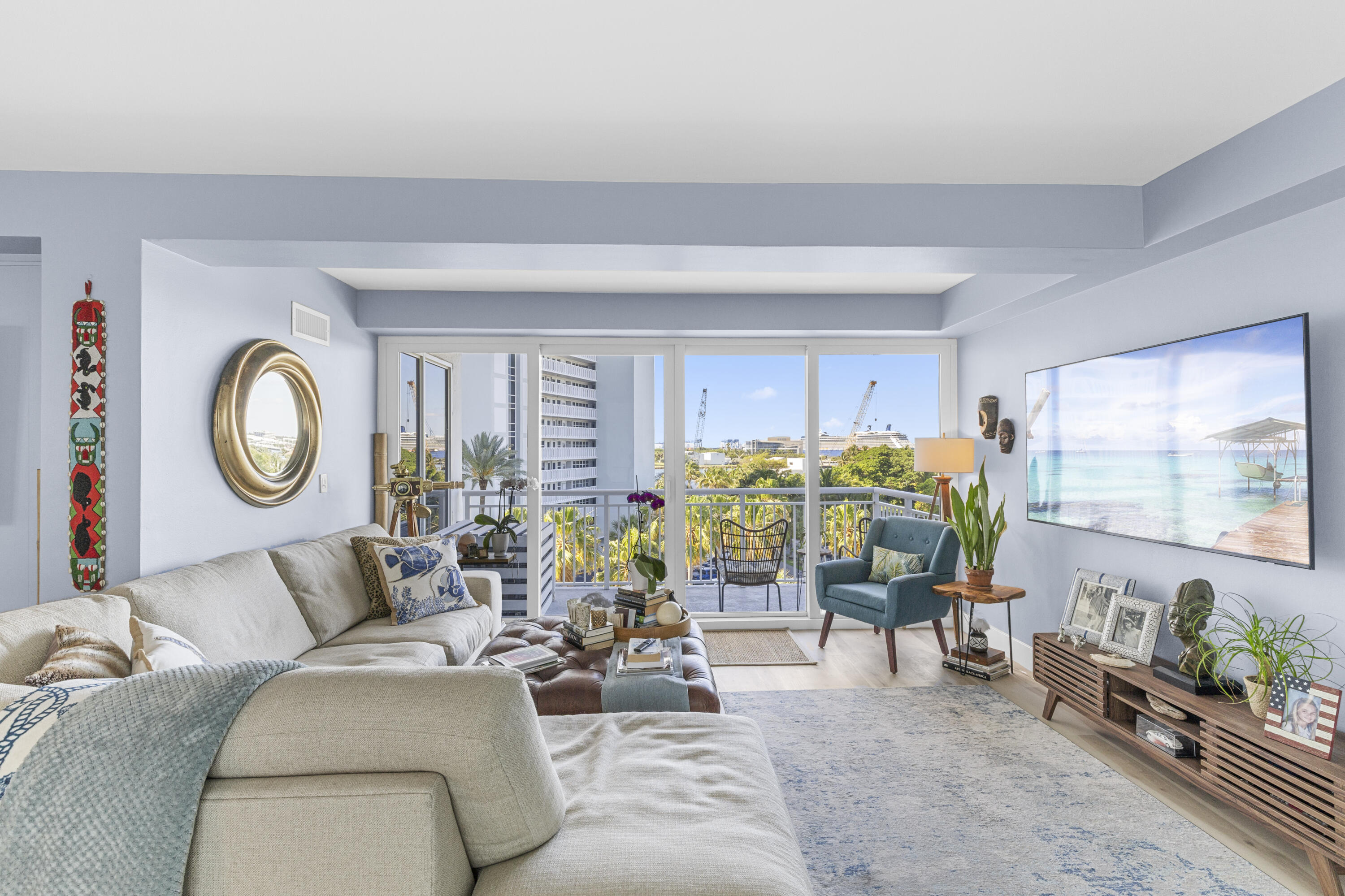 Furnished living room with a teal armchair and sliding doors opening to a palm-lined balcony.