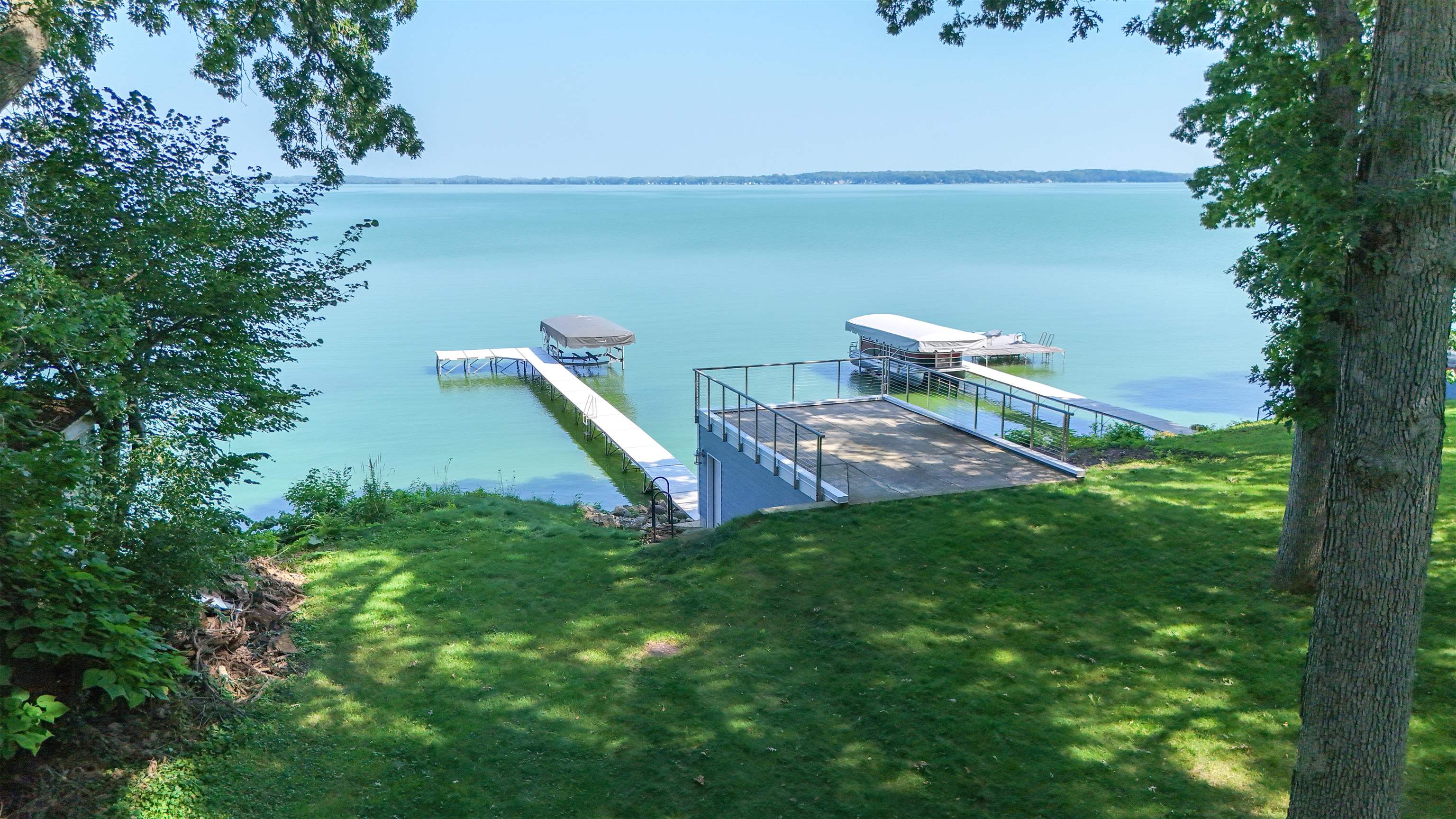 Lakefront lawn with two docks, covered boat lifts and a waterfront platform.