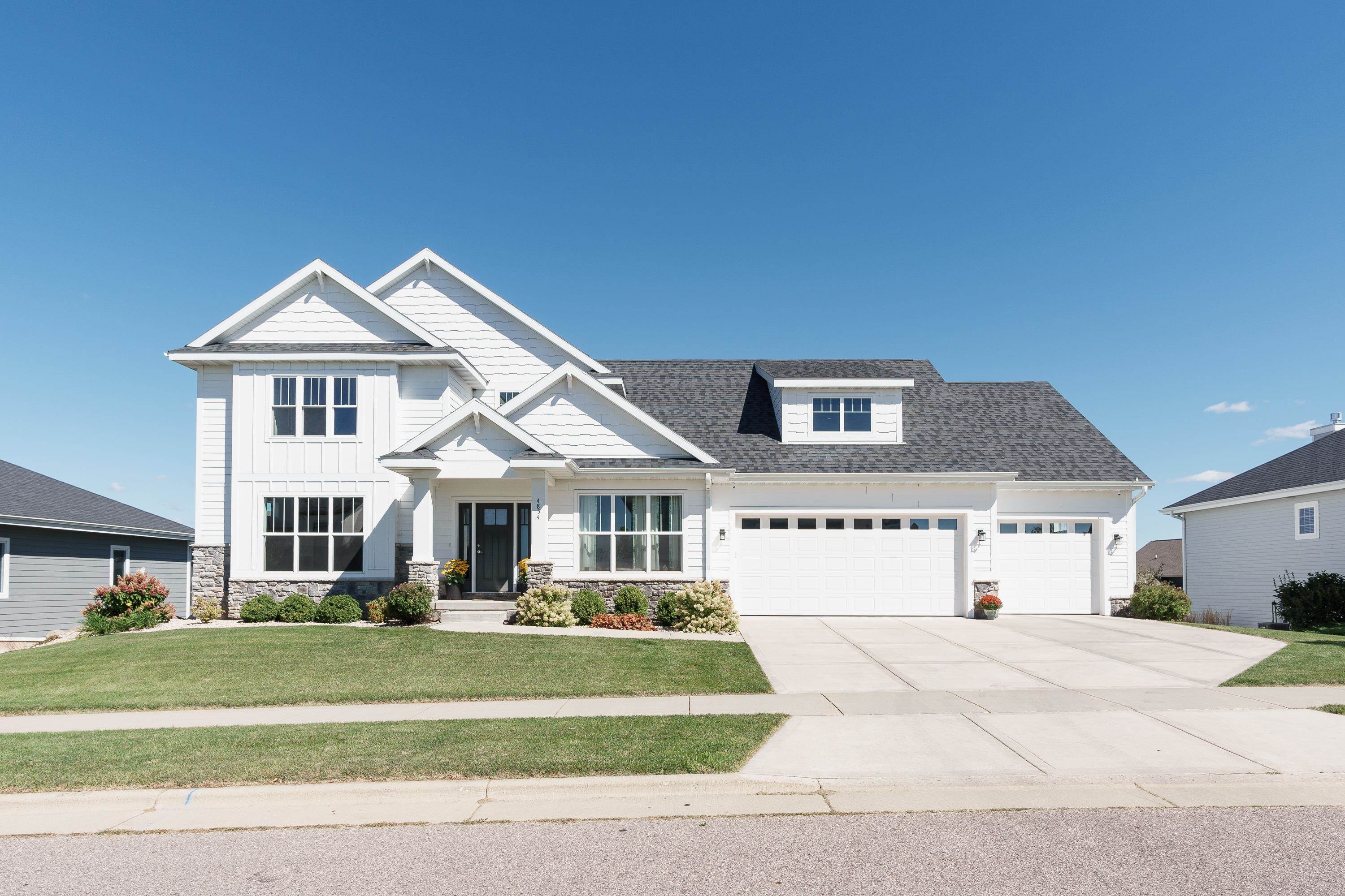 White two-story home with multiple gables, stone accents, and a three-car garage.