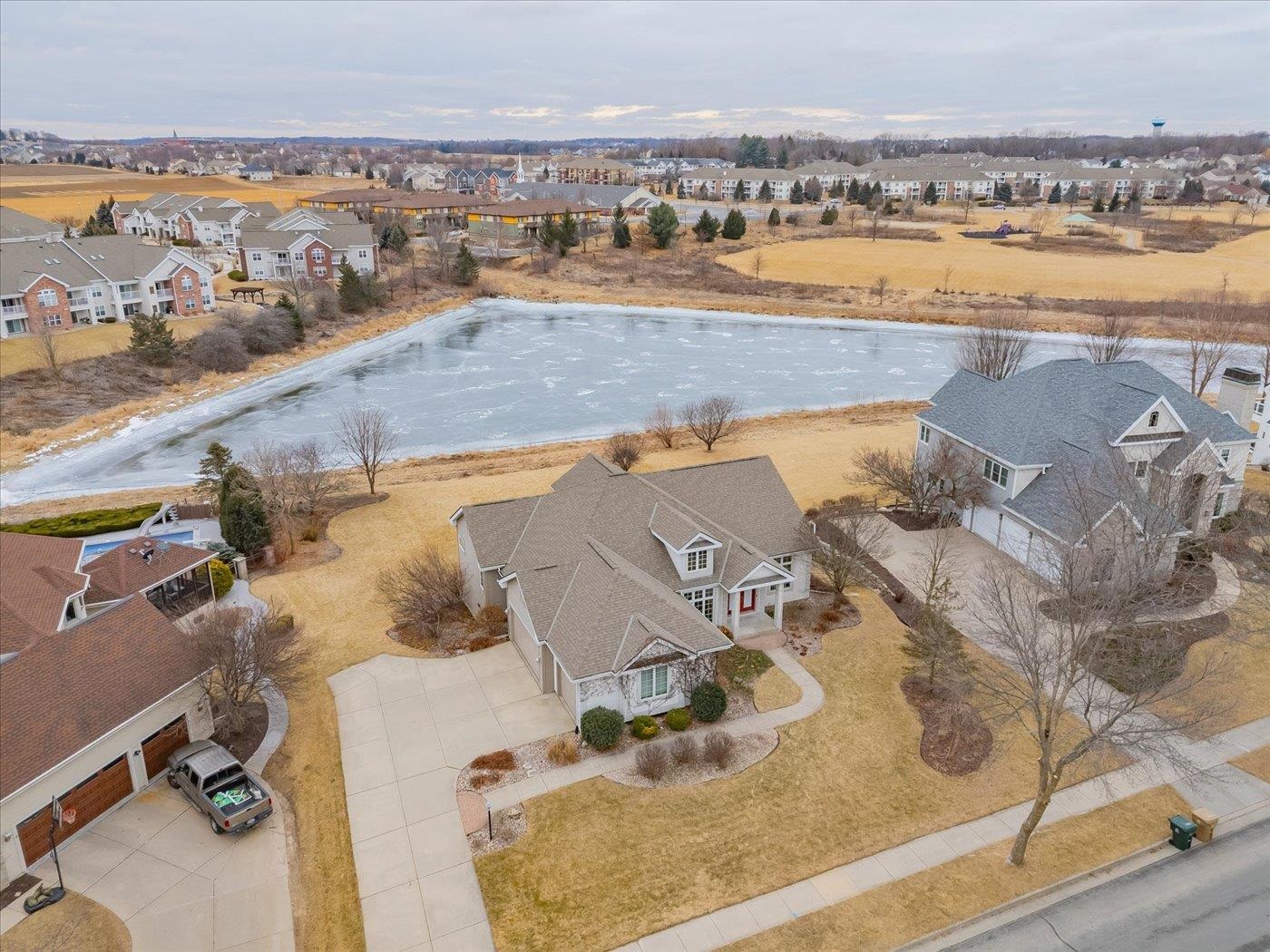 Aerial view of homes beside a frozen pond, with a house and driveway in the foreground.
