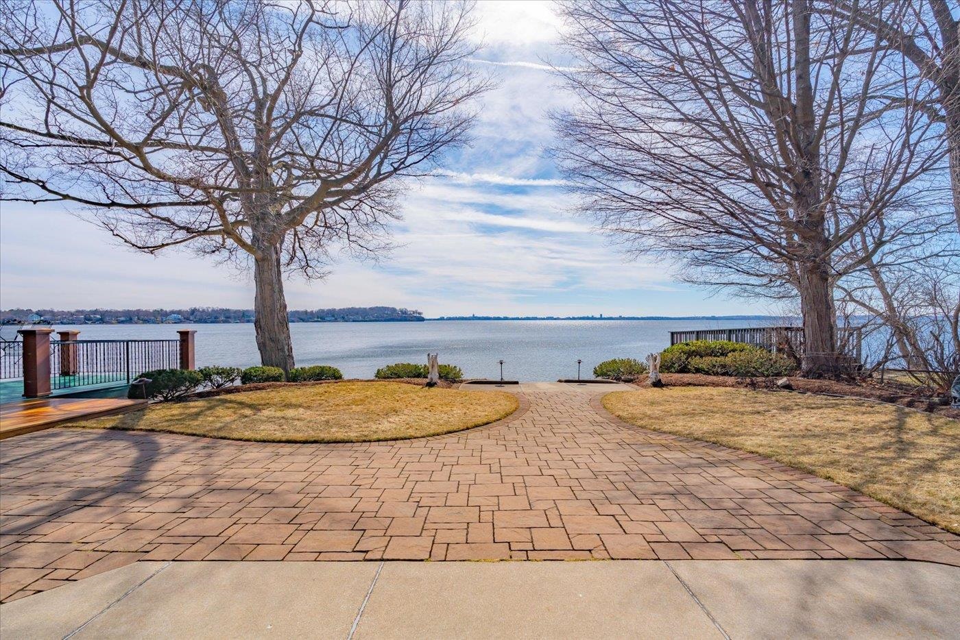 Waterfront patio with a broad brick terrace, curved lawn, and leafless trees.