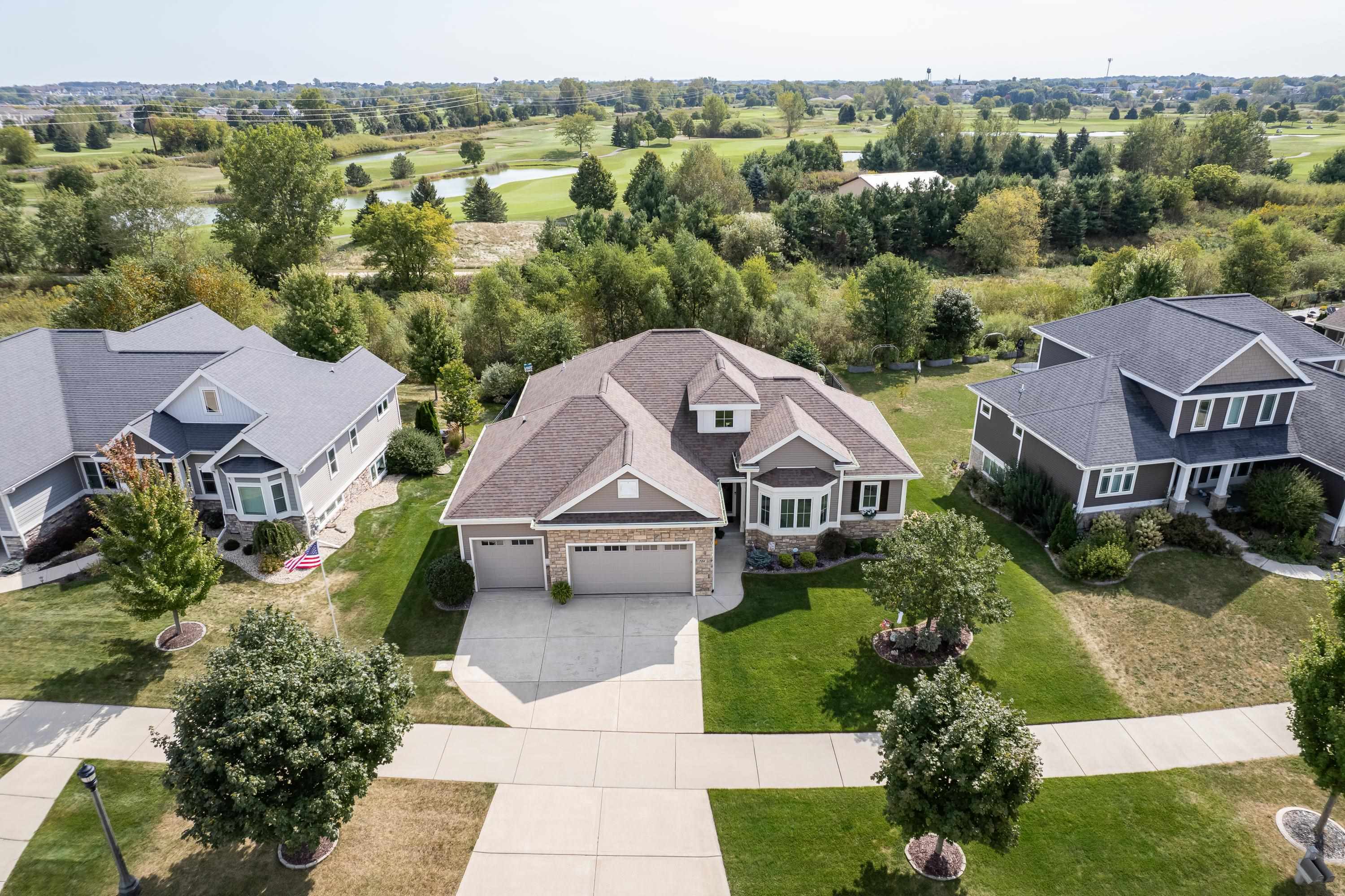 Aerial view of a suburban home beside a golf course, with neighboring houses and a pond beyond.