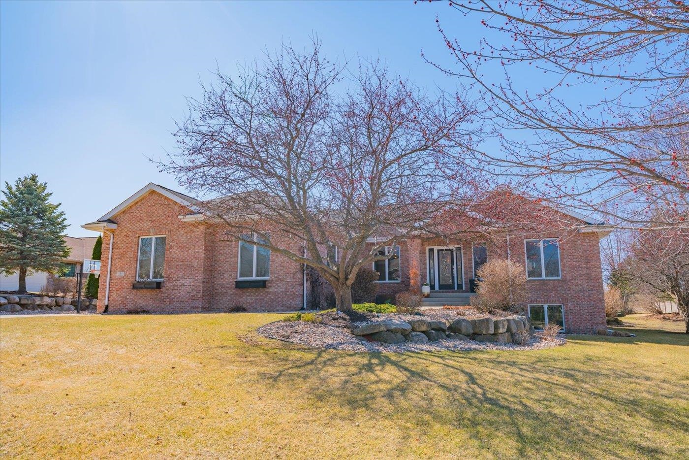 Red brick home with a large leafless tree shading the front lawn and stone-edged garden bed.