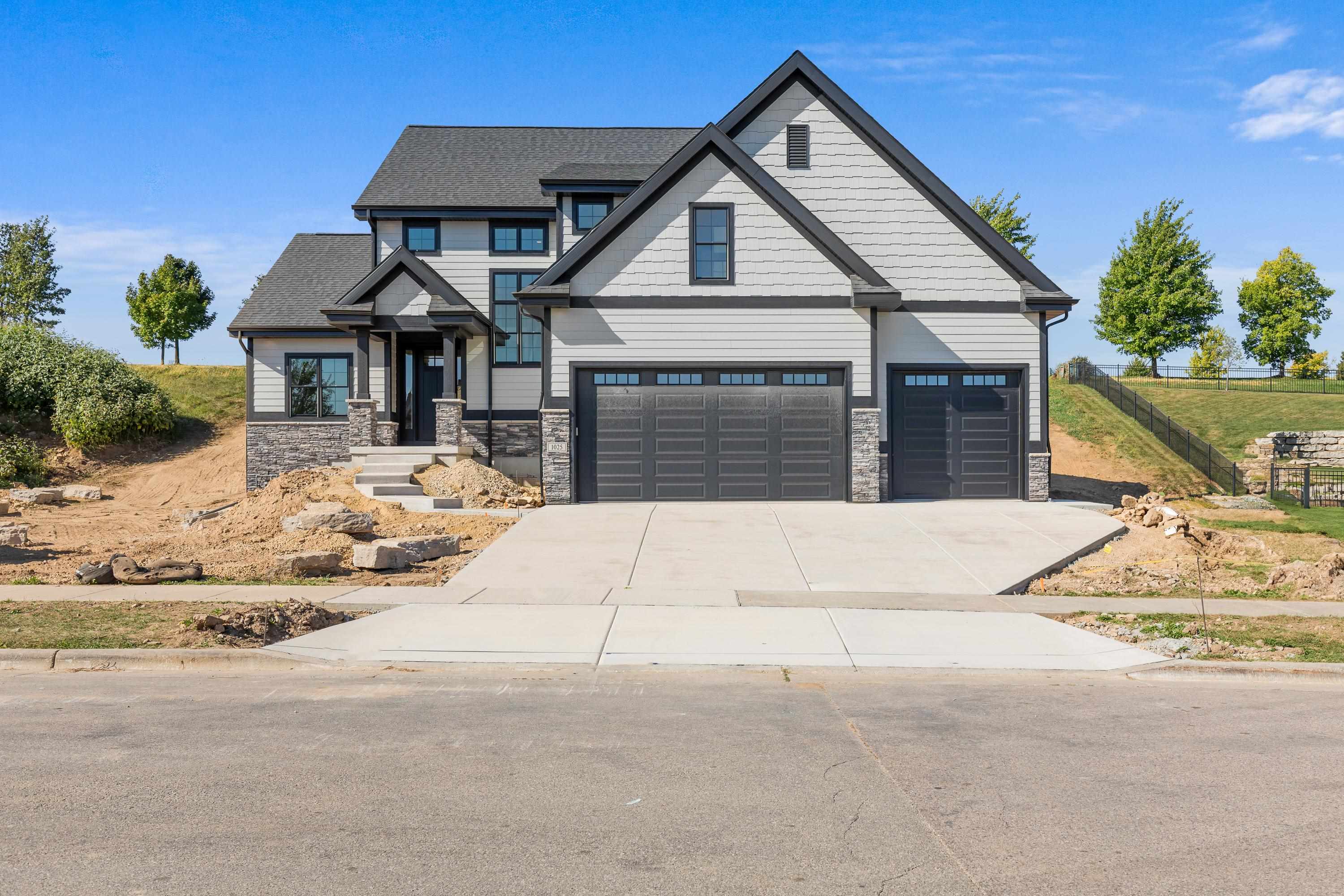 Gray two-story house with three dark garage doors, stone accents, and unfinished landscaping.