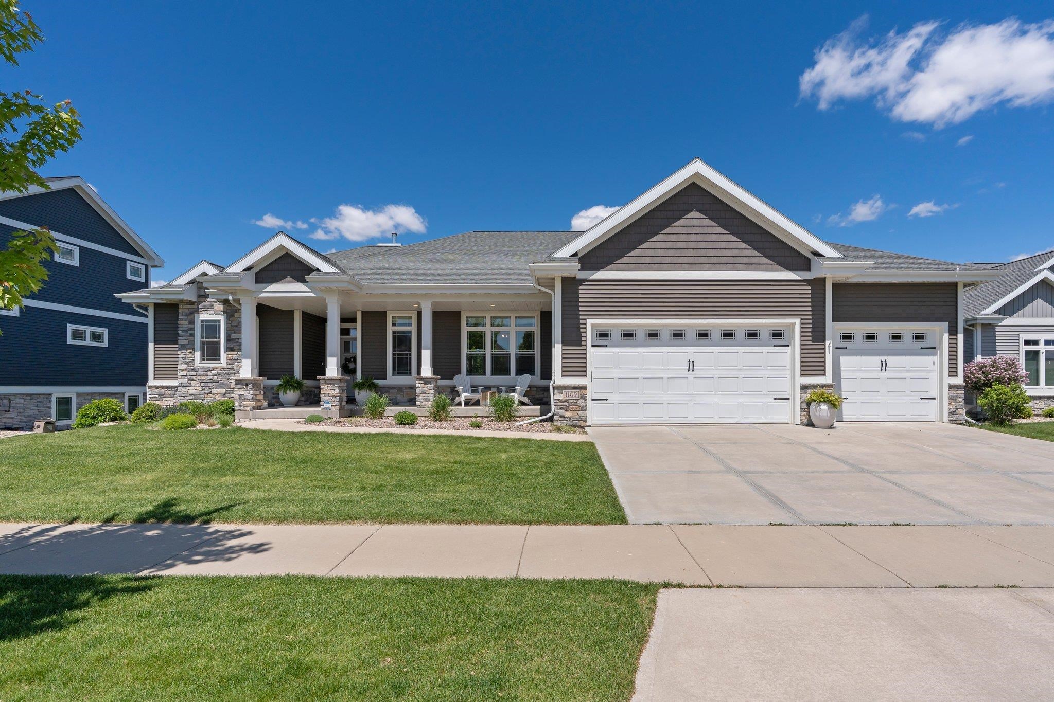 Gray single-story home with stone porch columns, a broad lawn, and two white garage doors.