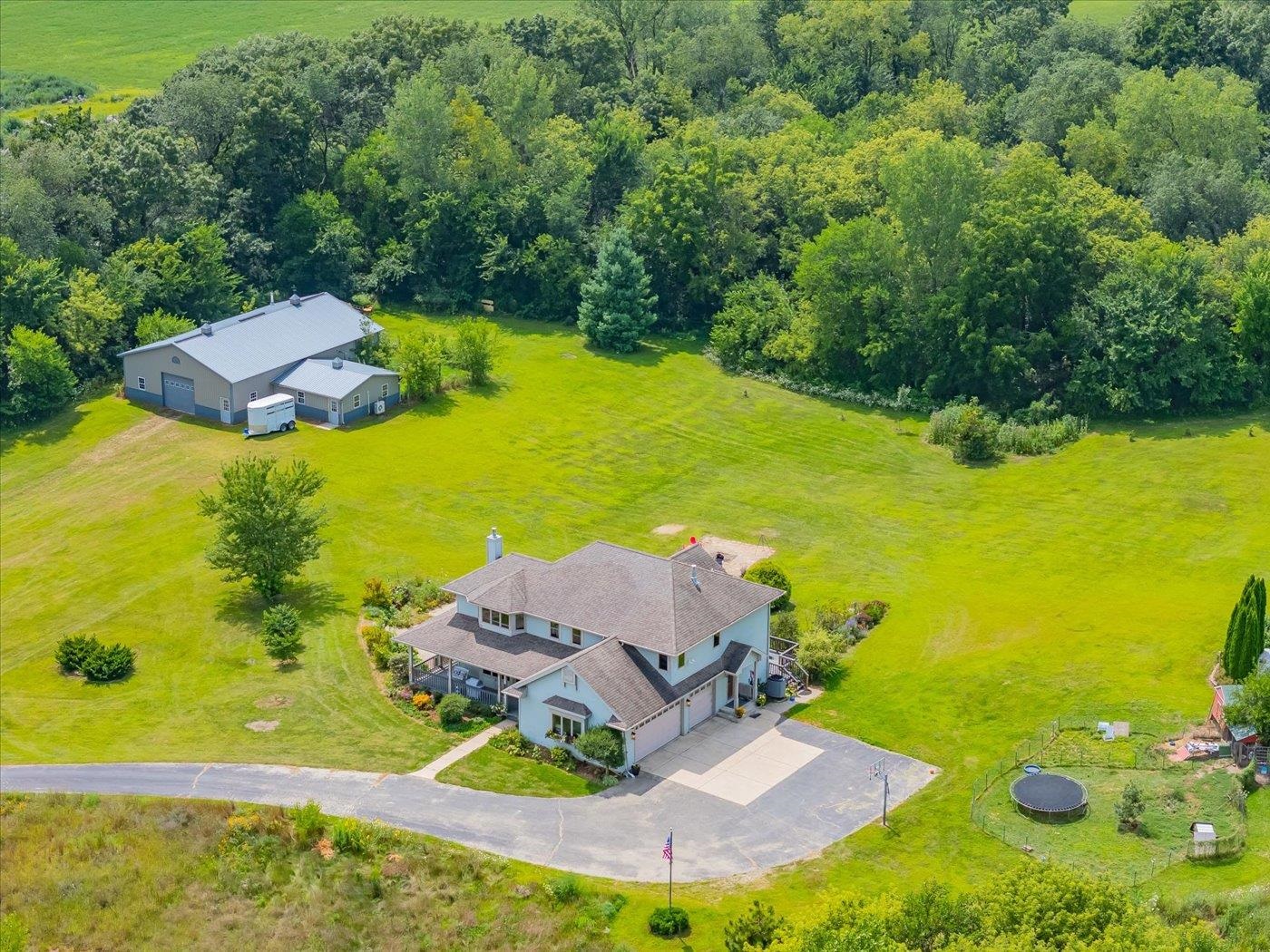 Aerial view of a rural home, separate outbuilding, broad lawn, and surrounding woods.