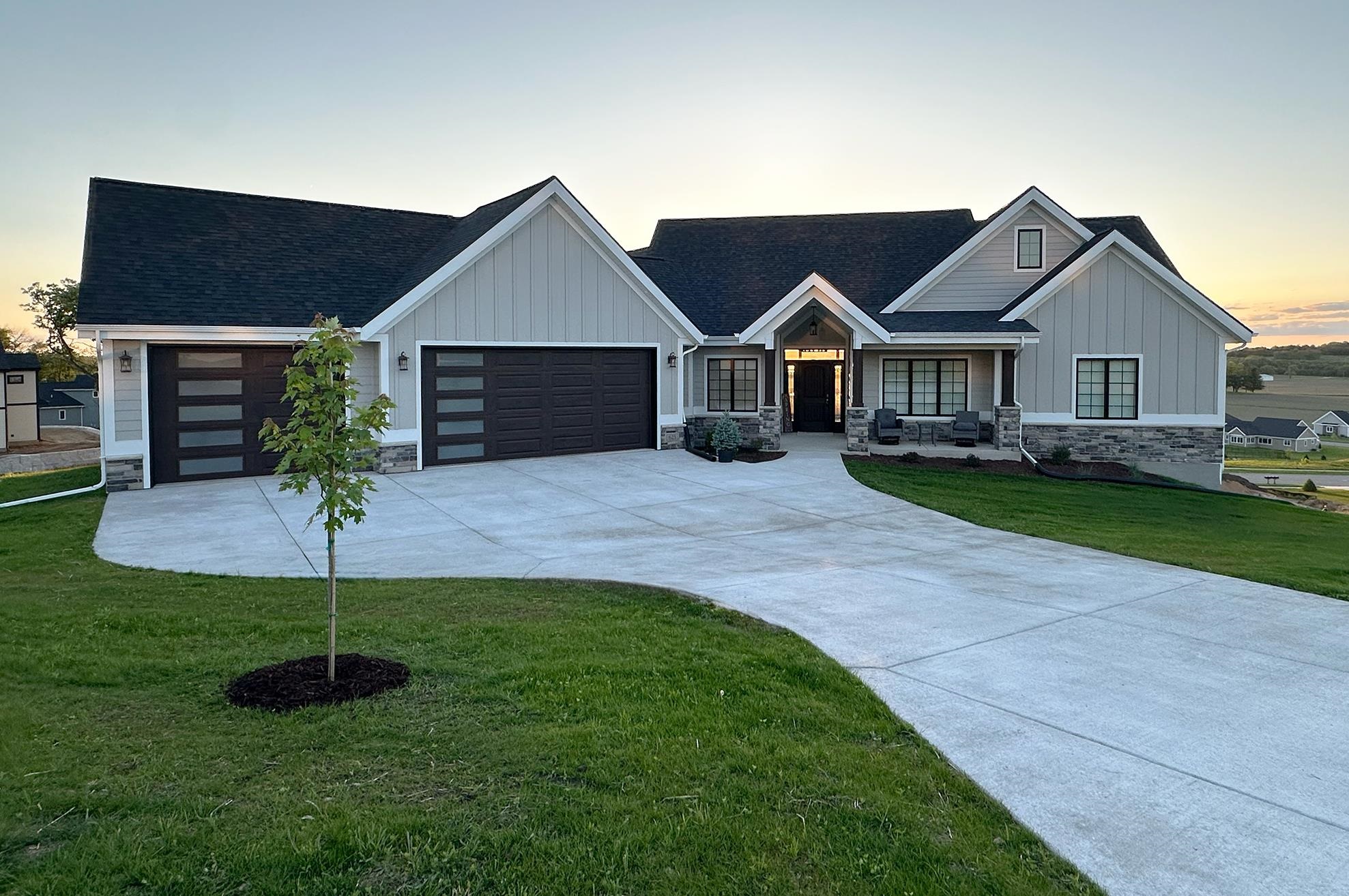 Light-gray home with multiple gables, stone accents, and a broad curved driveway at sunset.