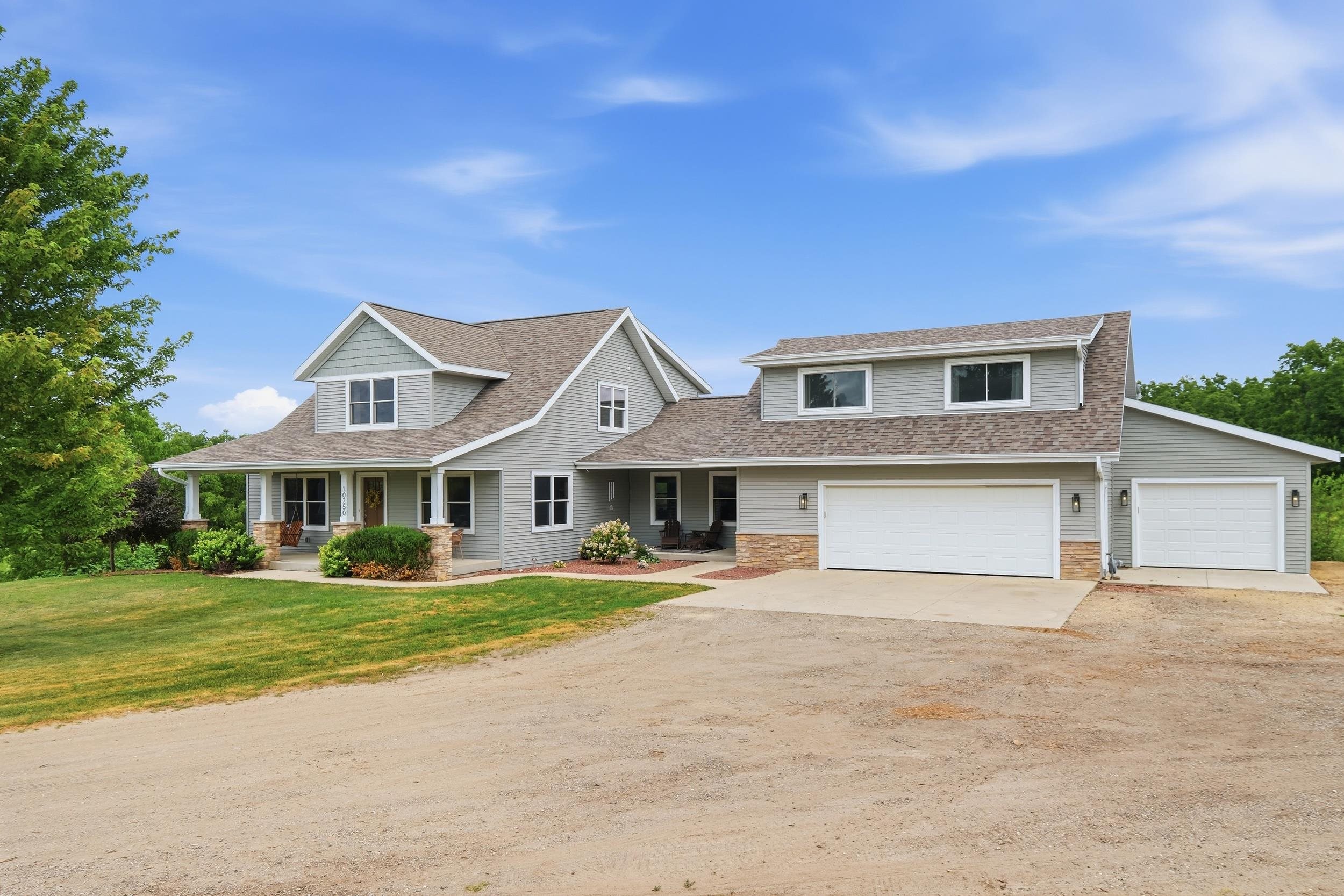 Gray multi-gabled home with a covered porch, two garage doors, and a broad gravel driveway.