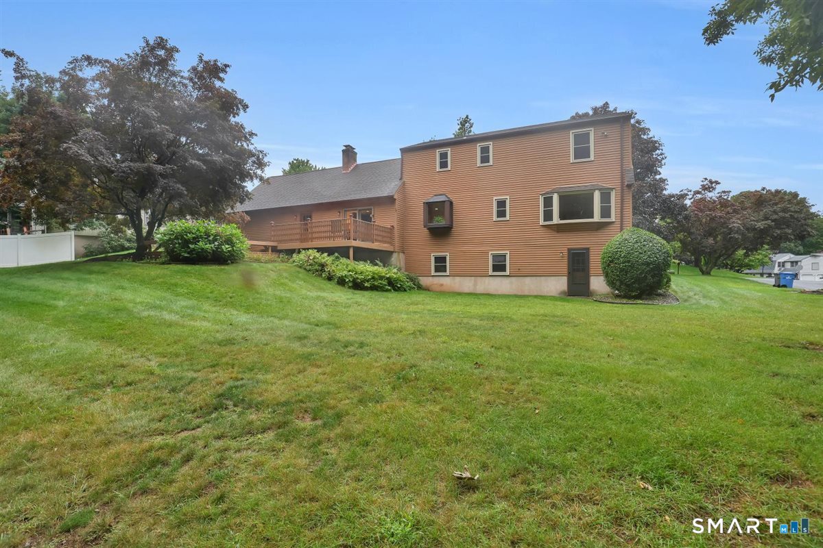 Rear exterior of a brown-sided home with a raised deck and broad sloping lawn.